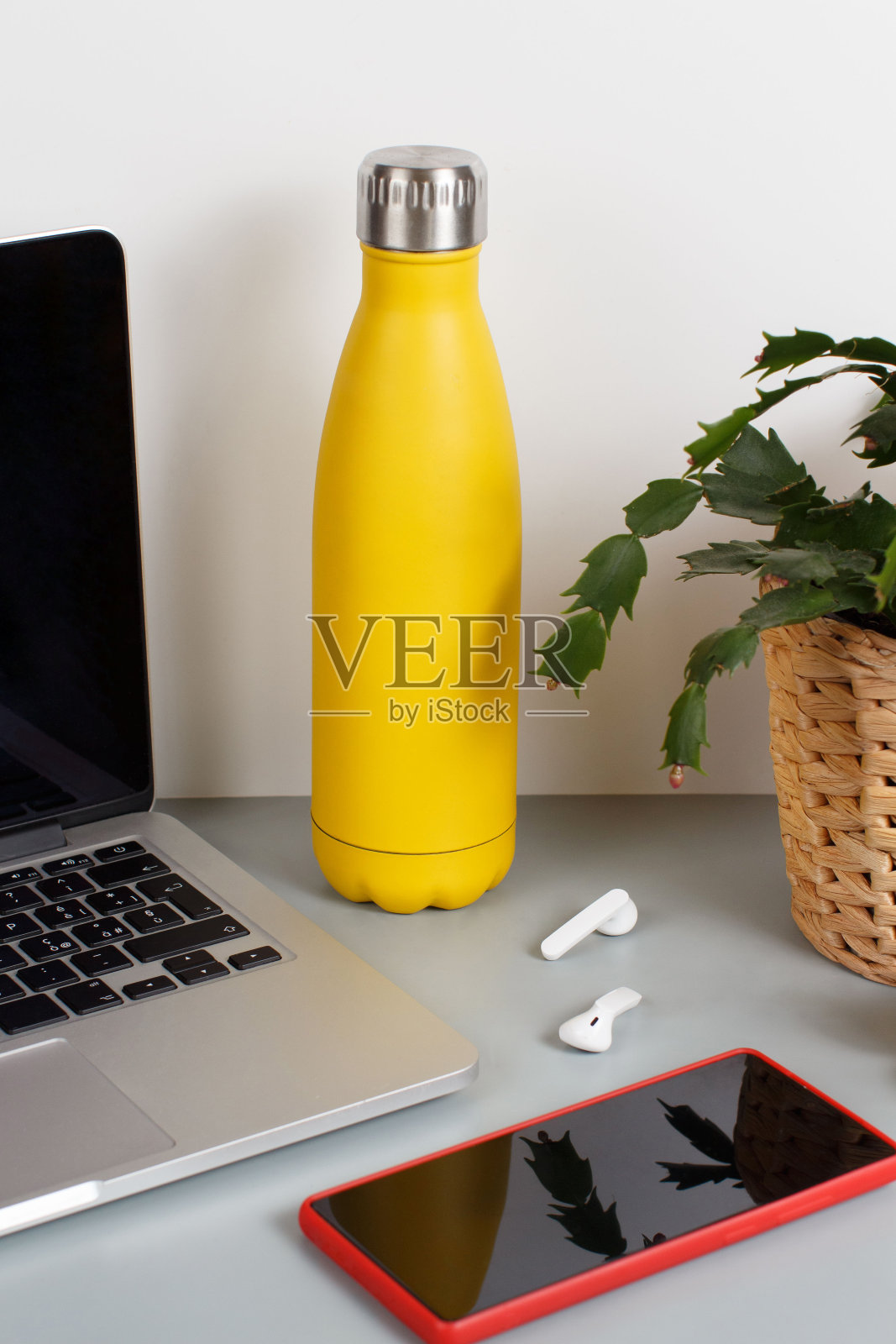 黄色的绝缘瓶放在灰色的桌子上，靠近现代的小器具和植物照片摄影图片