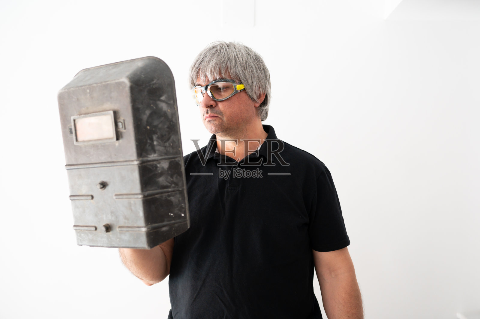 修理工拿着一个焊接保护面罩，用于家庭维修，在白色背景上绝缘。照片摄影图片