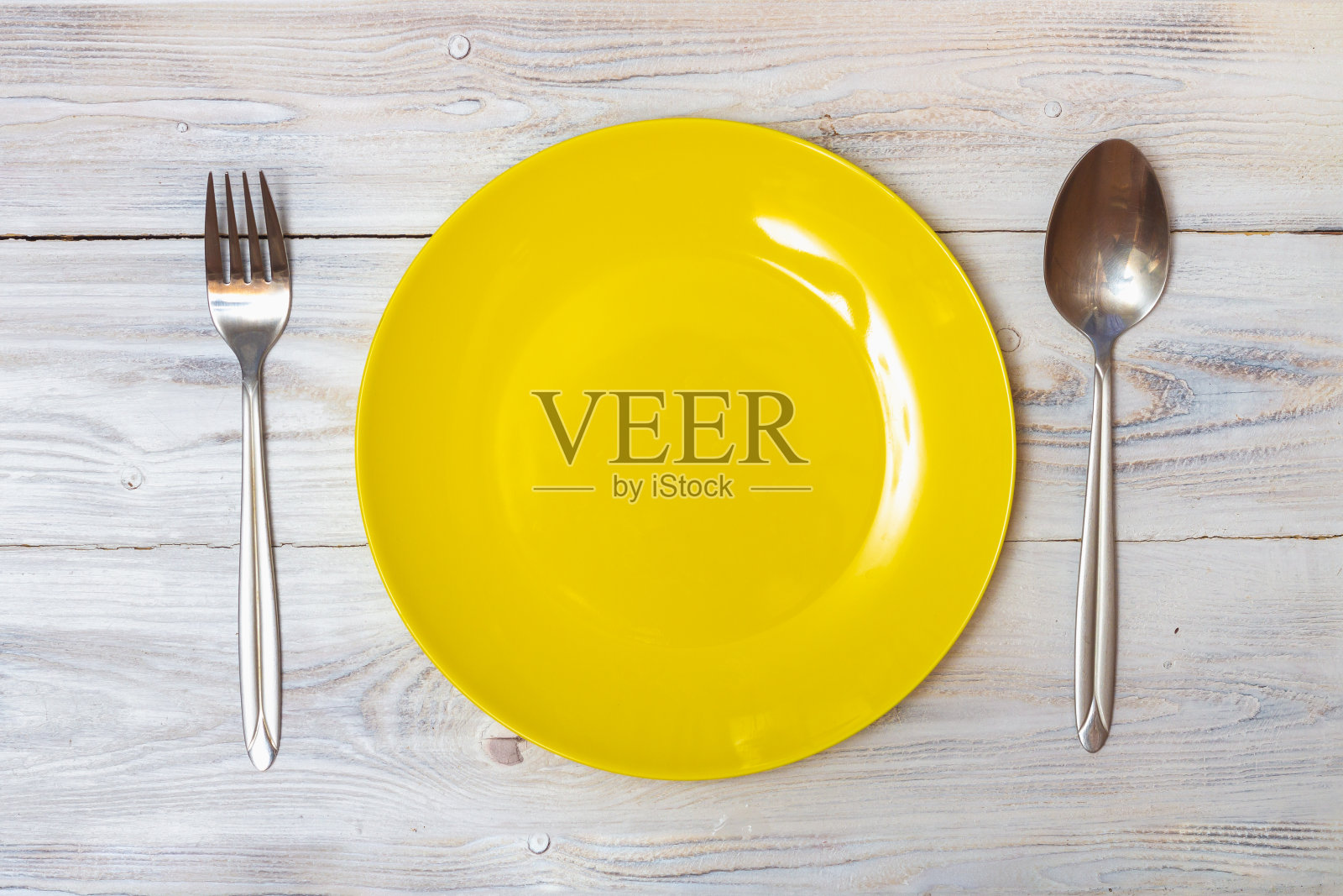 白色的桌子上放着一个没有食物的黄色空盘子，上面有勺子和叉子照片摄影图片