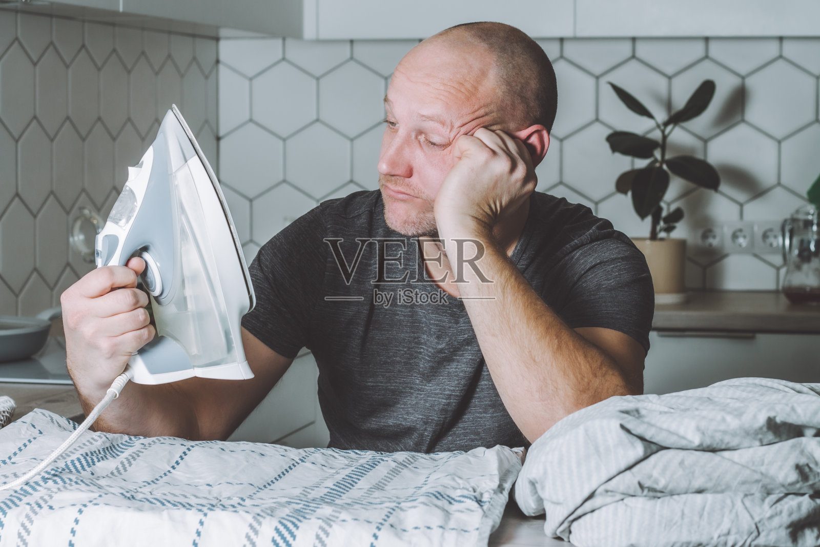 沉思的人看着熨斗和床单。父亲忙于做家务。照片摄影图片