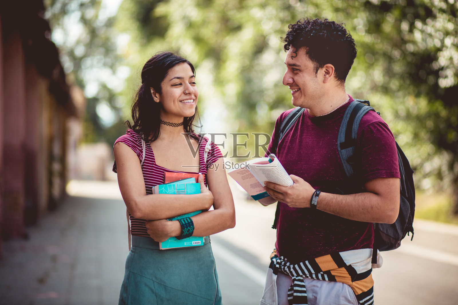 两个年轻的学生站在街上，拿着书聊天。照片摄影图片