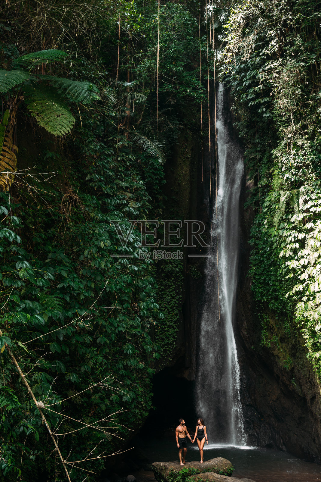 一对夫妇在热带瀑布。这对夫妇前往印度尼西亚的巴厘岛。一个女人和一个男人在美丽的瀑布旁。在热带岛屿上度假。一对在瀑布边旅行的夫妇照片摄影图片