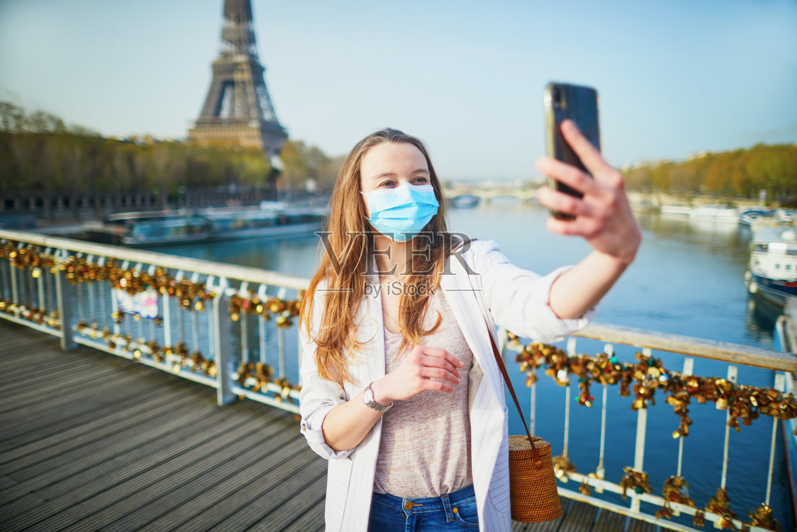 在冠状病毒爆发期间，一名年轻女孩站在巴黎埃菲尔铁塔附近，戴着防护口罩照片摄影图片