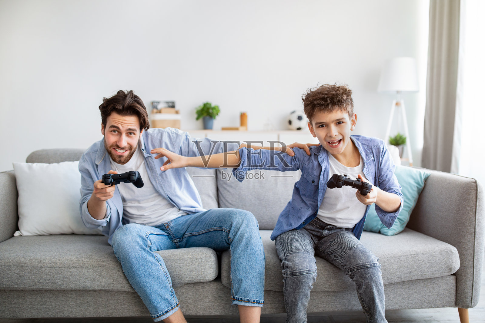 休闲活动的概念。快乐的父亲和儿子在玩电子游戏中竞争，互相推动照片摄影图片