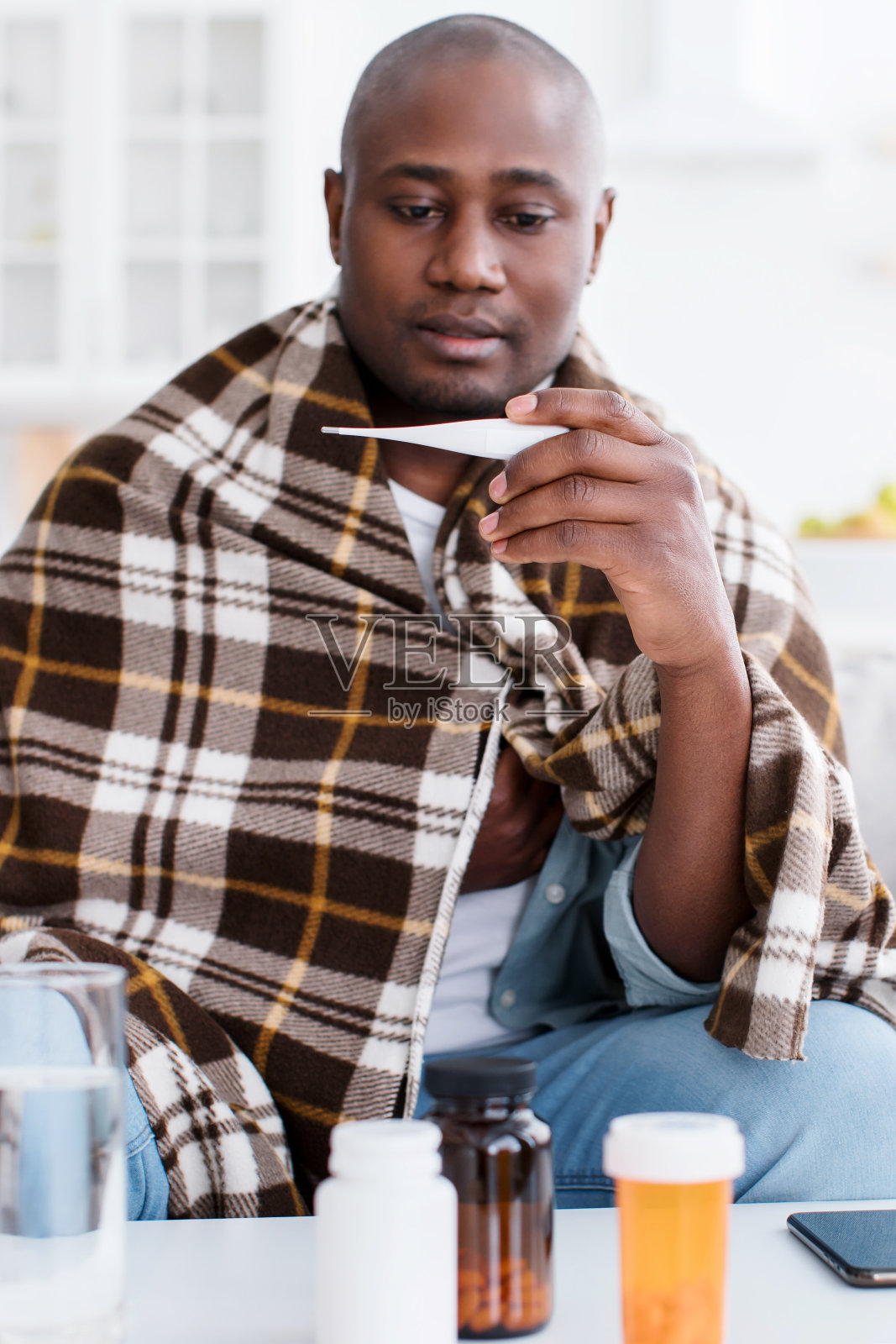 发烧和疾病。生病的黑人忍受着高烧，拿着体温计，裹在毯子里照片摄影图片