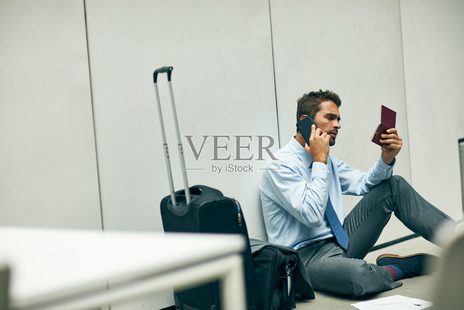 一名年轻英俊的商人坐在机场候机楼里，拿着护照使用手机照片摄影图片