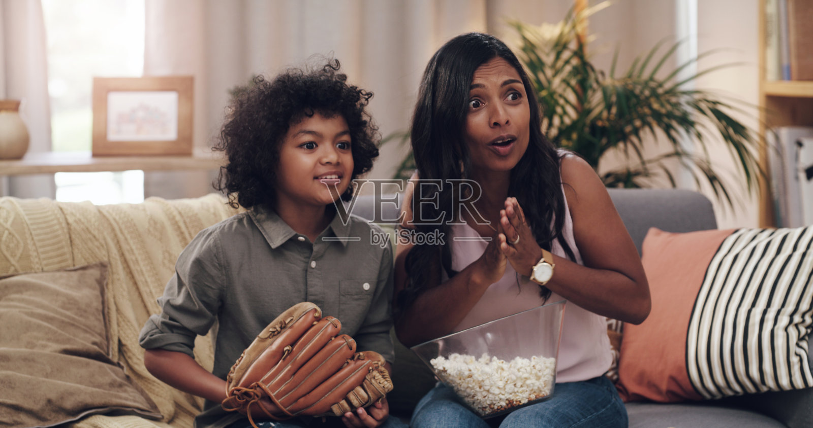 一个可爱的小男孩和他的妈妈在家里看棒球比赛照片摄影图片