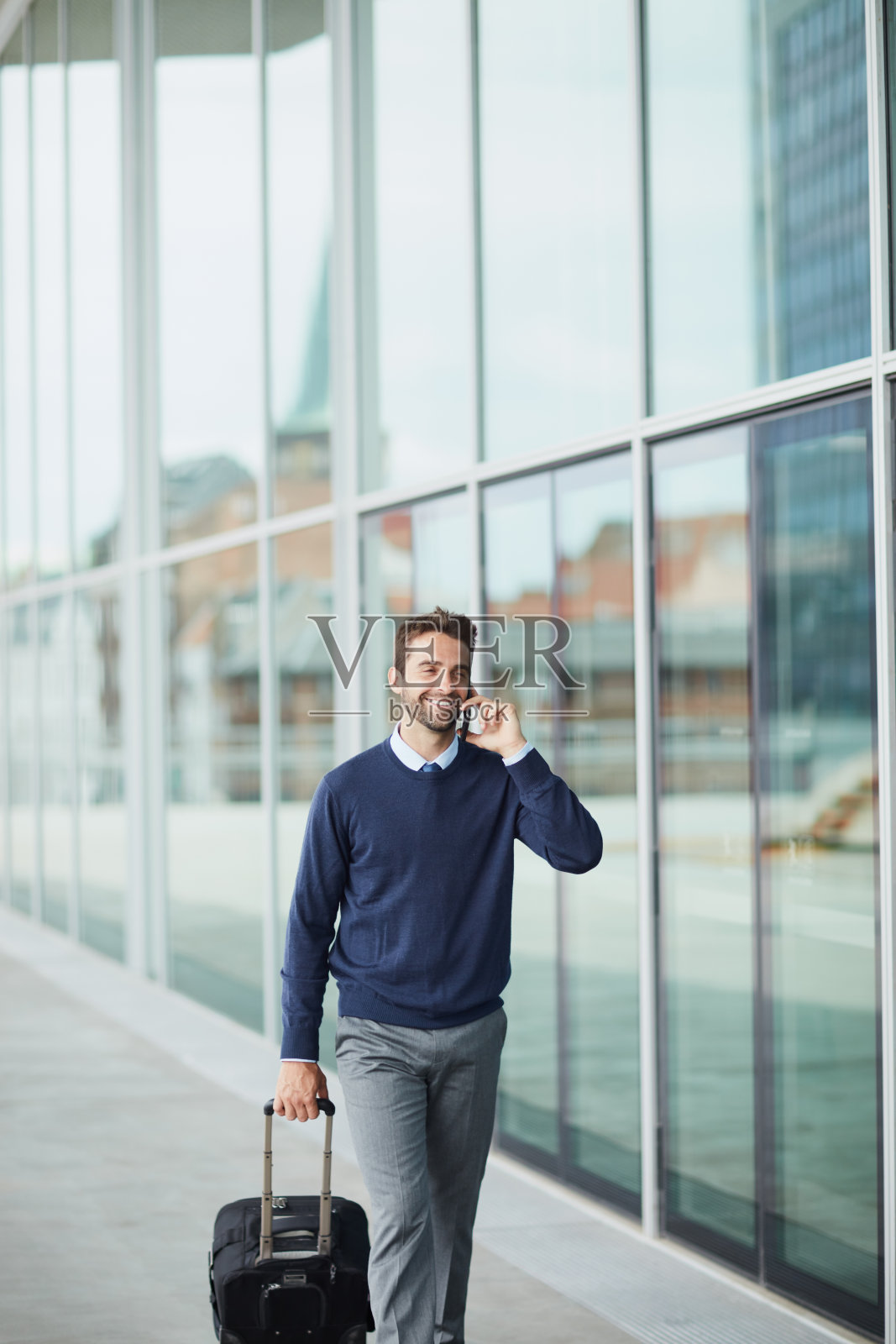 一名英俊的年轻商人在移动中提着一个手提箱，同时在白天使用他的手机照片摄影图片