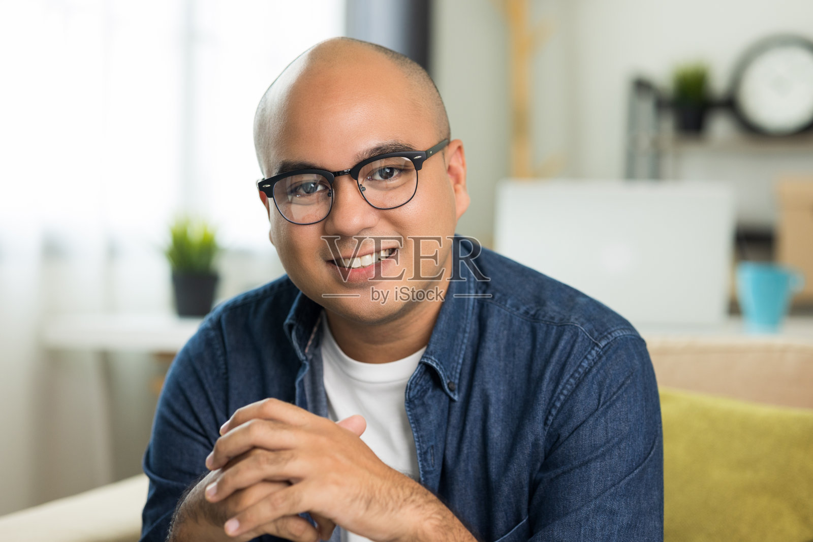 年轻英俊的印度男子戴着眼镜坐在客厅的沙发上。照片摄影图片