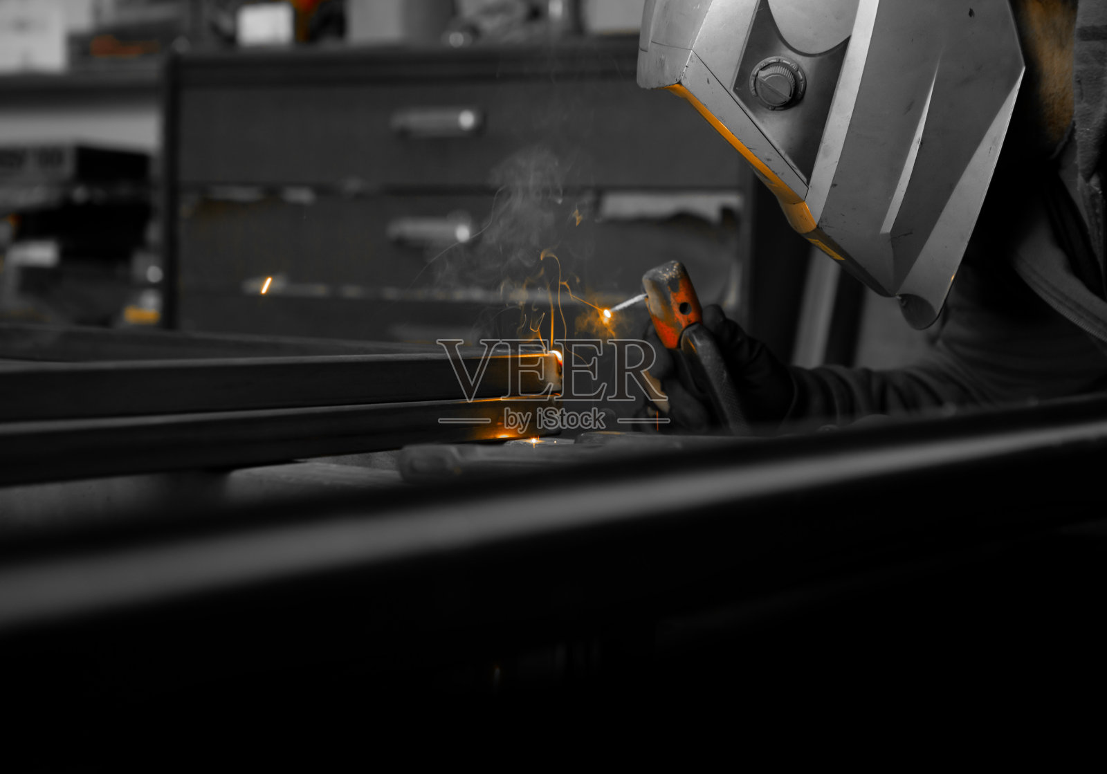 一个头上戴着保护面罩的人在车间里焊接管子。照片摄影图片