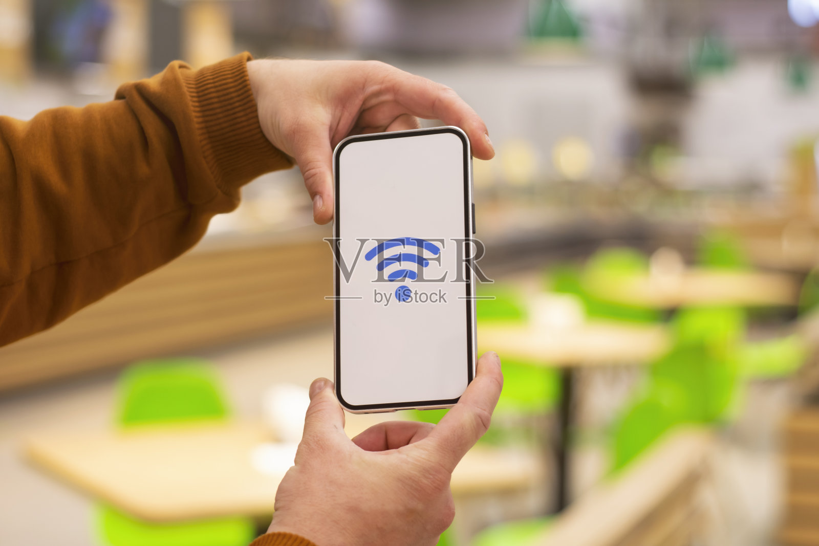 免费的无线网络。带有wi-fi图标的手机显示器，背景是一家餐厅。男子手里拿着一部智能手机。照片摄影图片