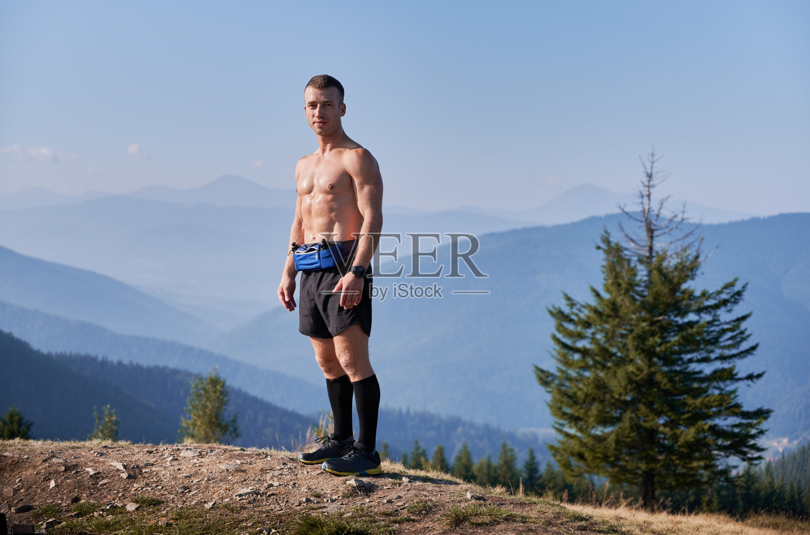 英俊的运动员站在山顶上。照片摄影图片