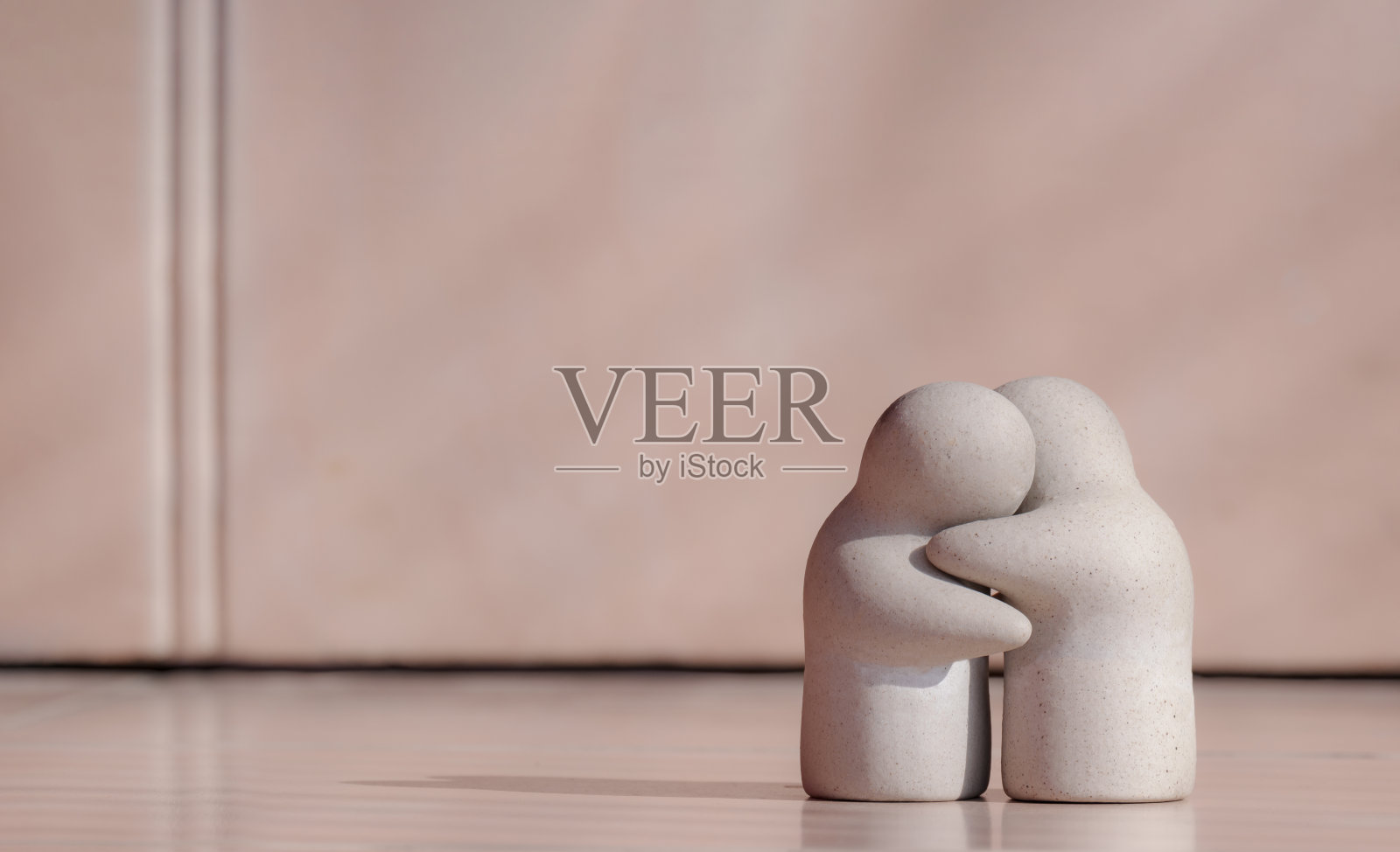 迷你花园观赏性人玩偶在拥抱姿态瓷砖地板与模糊的粉红色墙壁背景在关怀，爱和鼓励的概念照片摄影图片