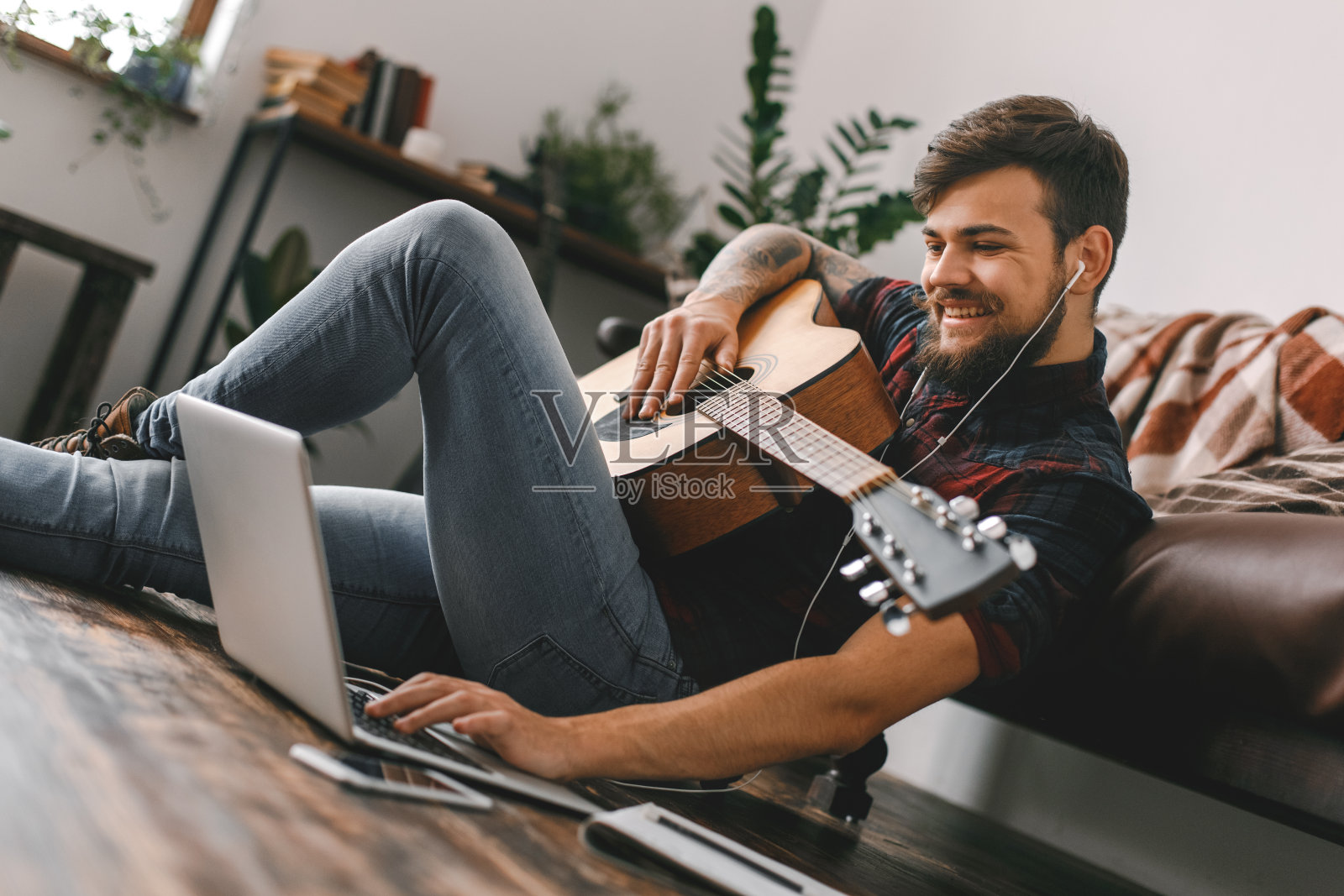 年轻的吉他手潮人坐在家里的地板上拿着吉他耳机音乐浏览笔记本电脑照片摄影图片