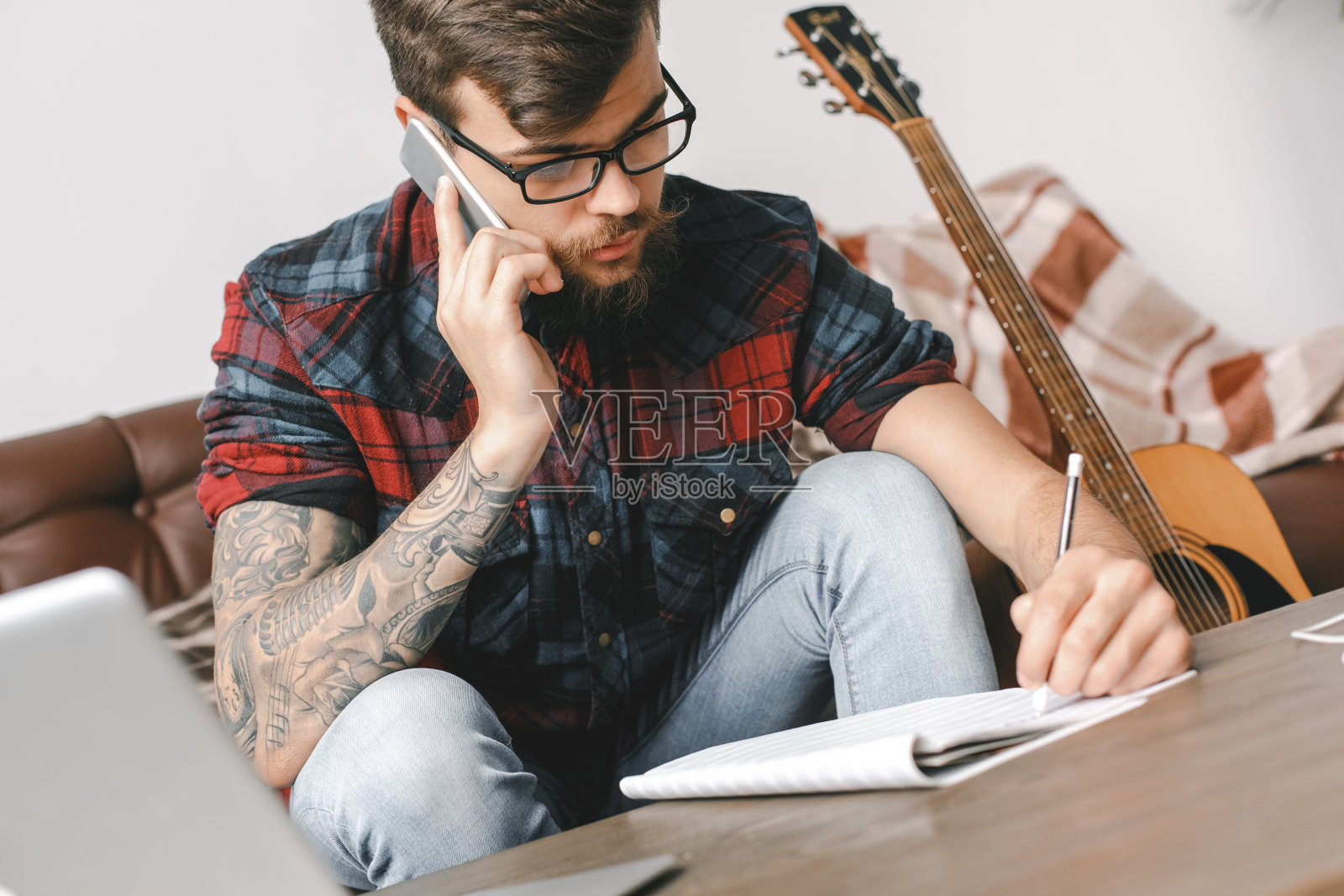 年轻的吉他手潮人在家与吉他坐写歌曲电话特写照片摄影图片