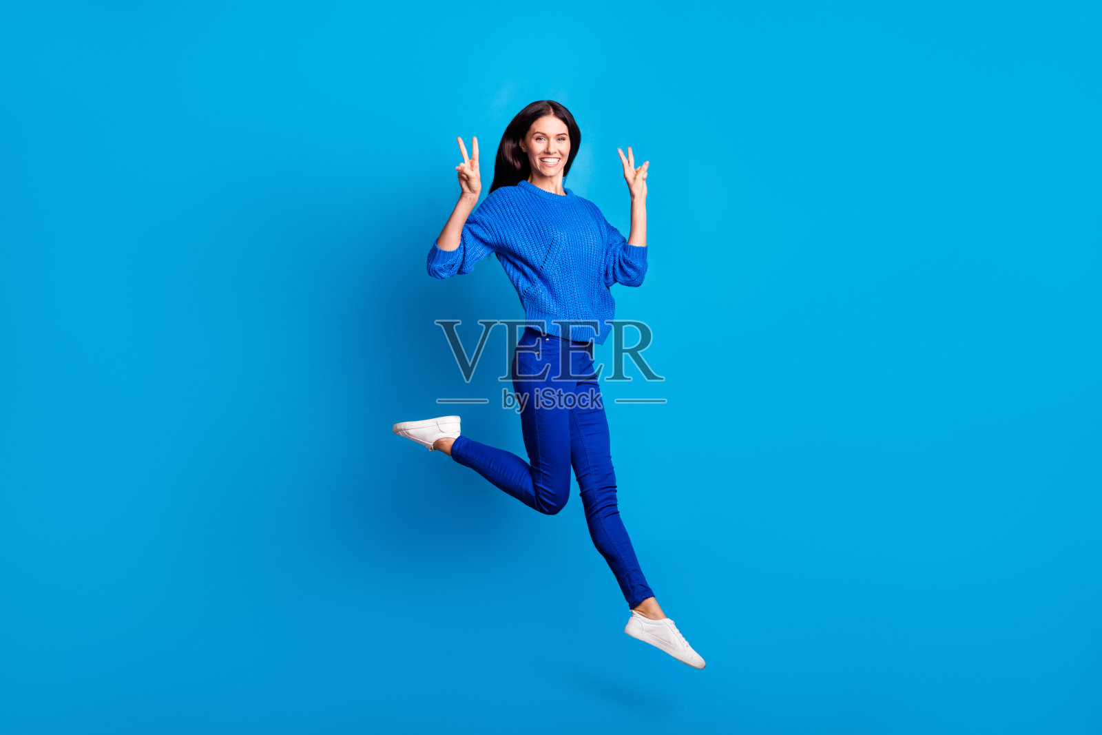 全尺寸的档案照片乐观可爱的女士跳显示v标志，穿毛衣，裤子，运动鞋孤立在明亮的背景照片摄影图片