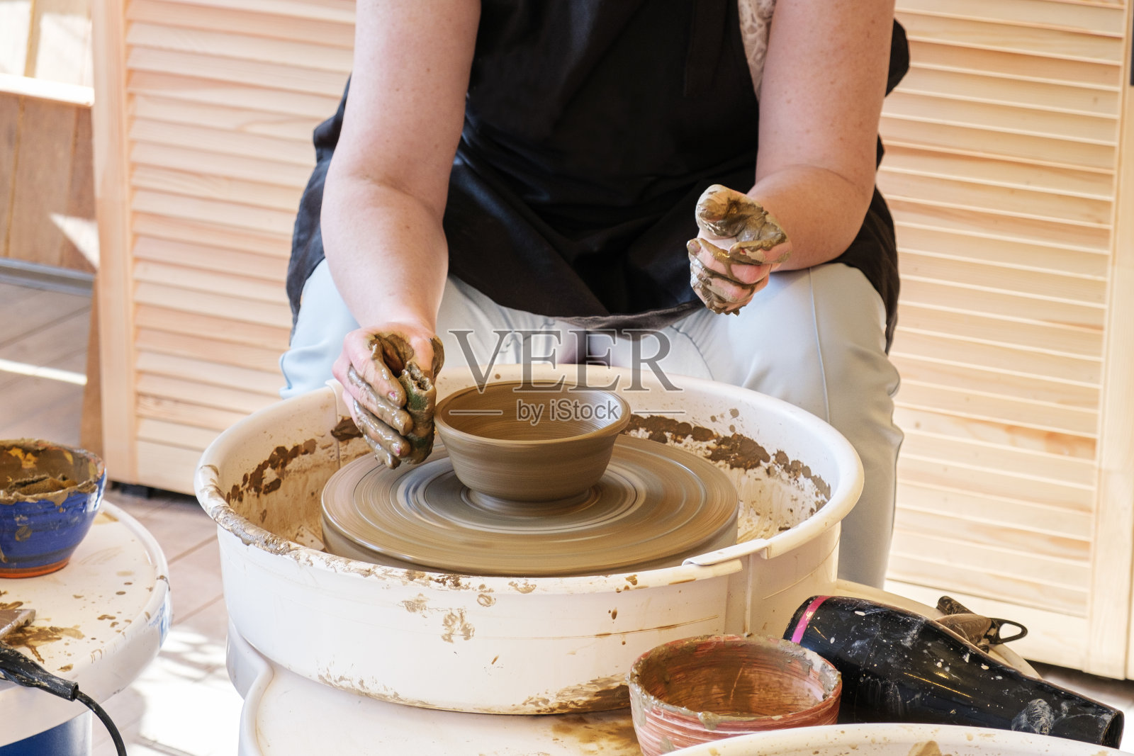 女人在小陶工轮上制作陶土盘子。陶艺工作室的大师班。照片摄影图片