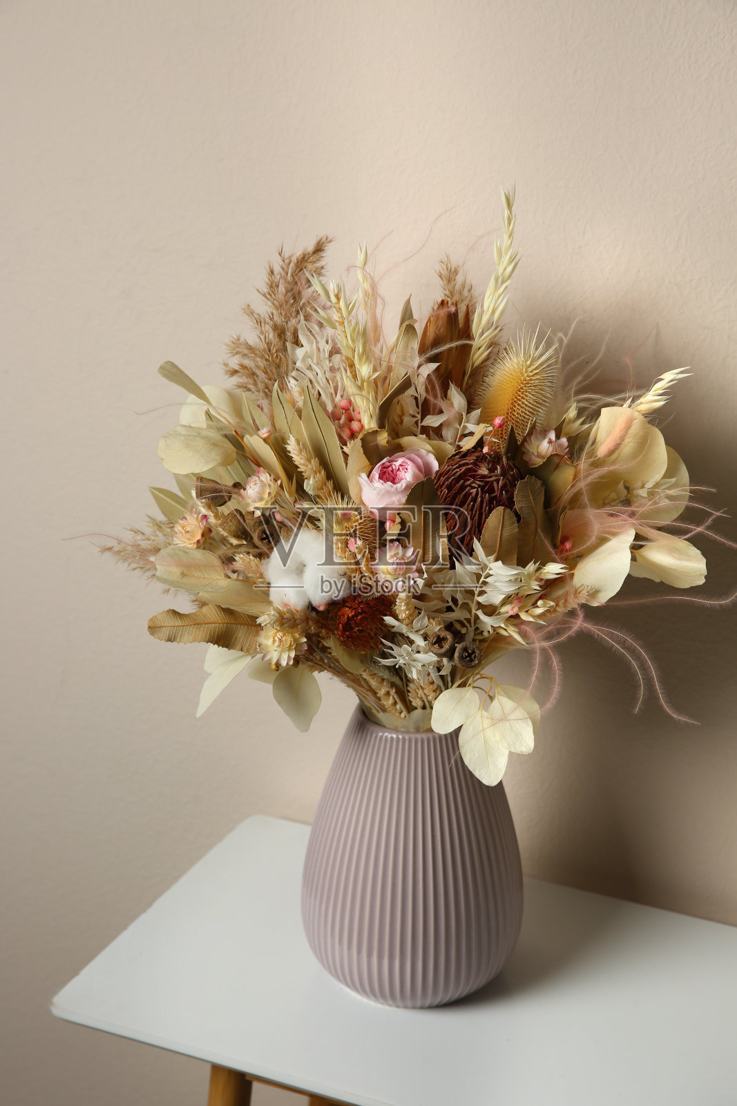 漂亮的干花花束插在瓷瓶里，放在浅灰色的墙上白色的桌子上照片摄影图片