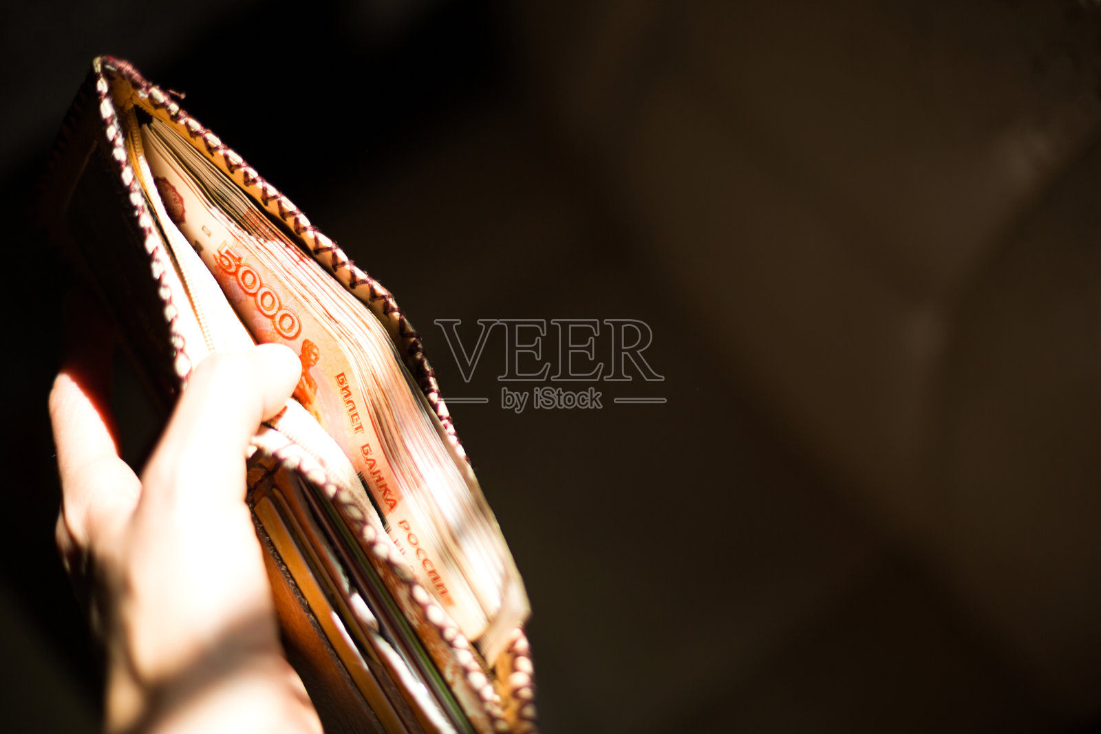 装满俄罗斯钱的皮夹5000张纸币，5000卢布。在一束光的背景下，一名男子的手握着一个打开的、溢出的钱包。本空间照片摄影图片