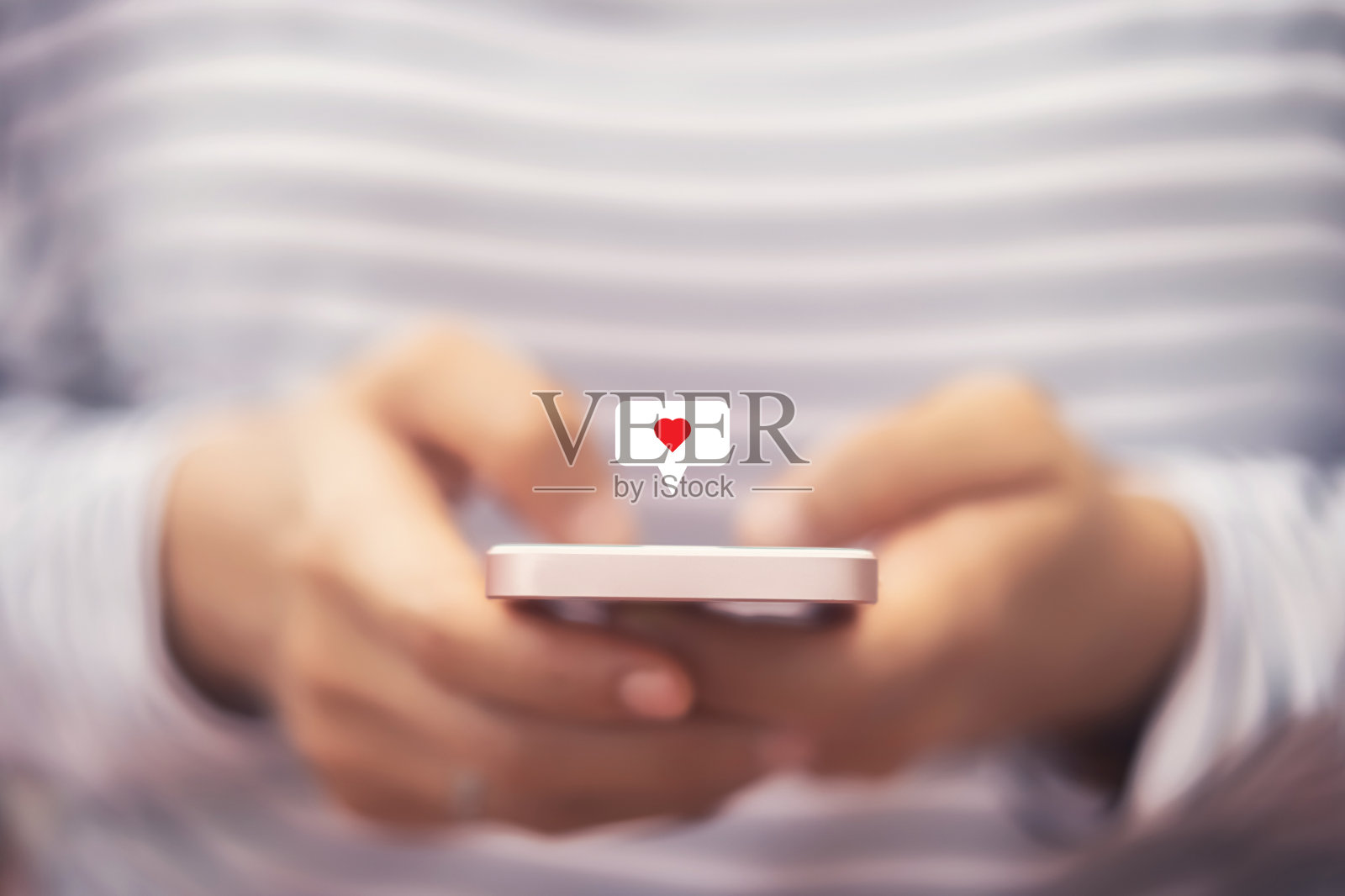 靠近女人的手握使用智能手机与心脏图标在户外公园街道的背景。照片摄影图片