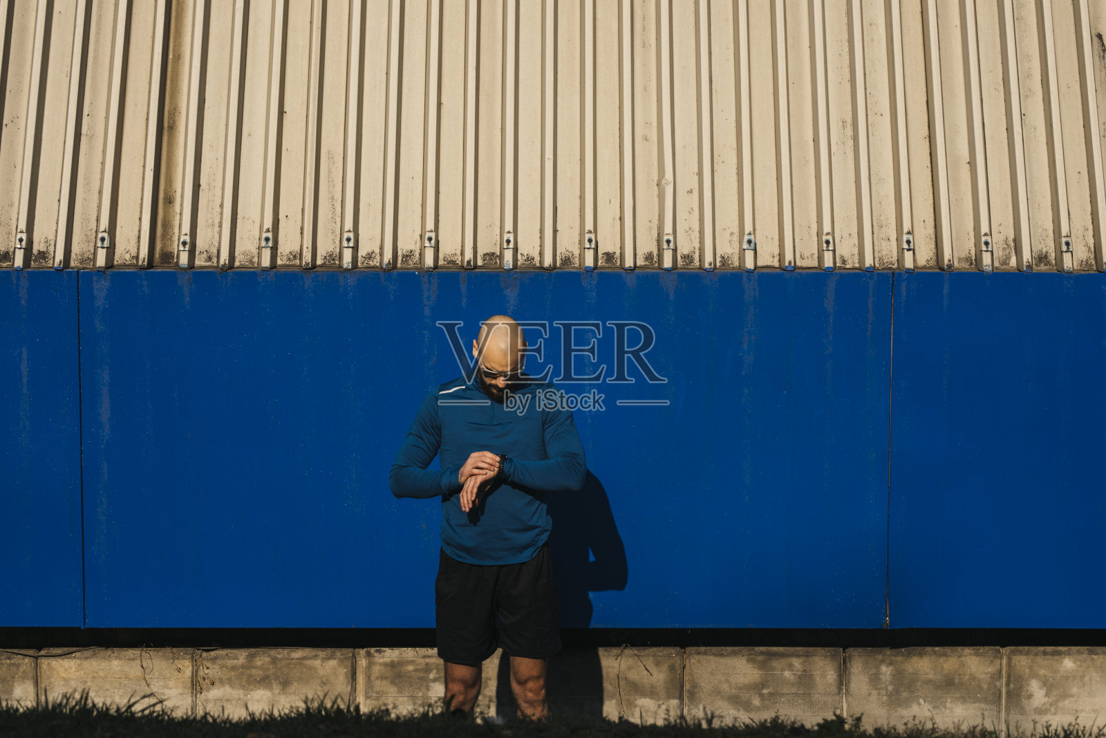 帅气的光头运动员戴着太阳镜在公共场所锻炼时用智能手表测量脉搏(城市环境)照片摄影图片