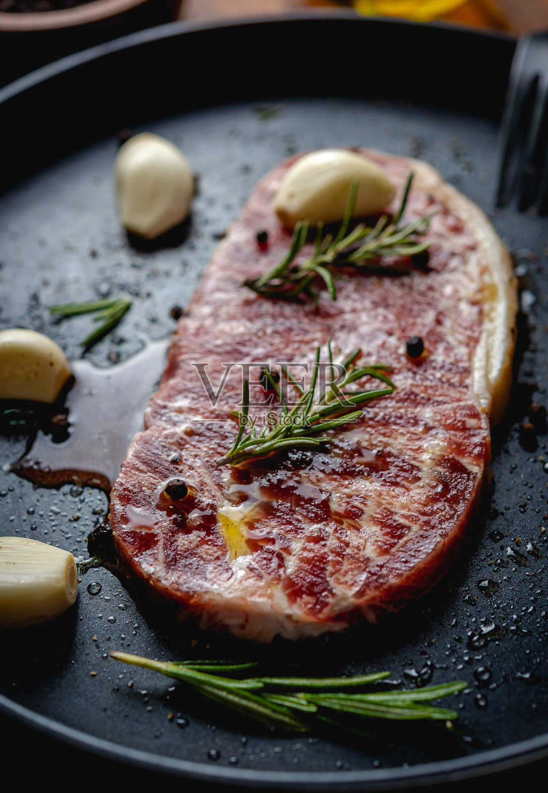 新鲜的生牛排配上橄榄油，彩色的胡椒，大蒜和迷迭香叶，放在黑色托盘上的木桌上，俯视图。照片摄影图片