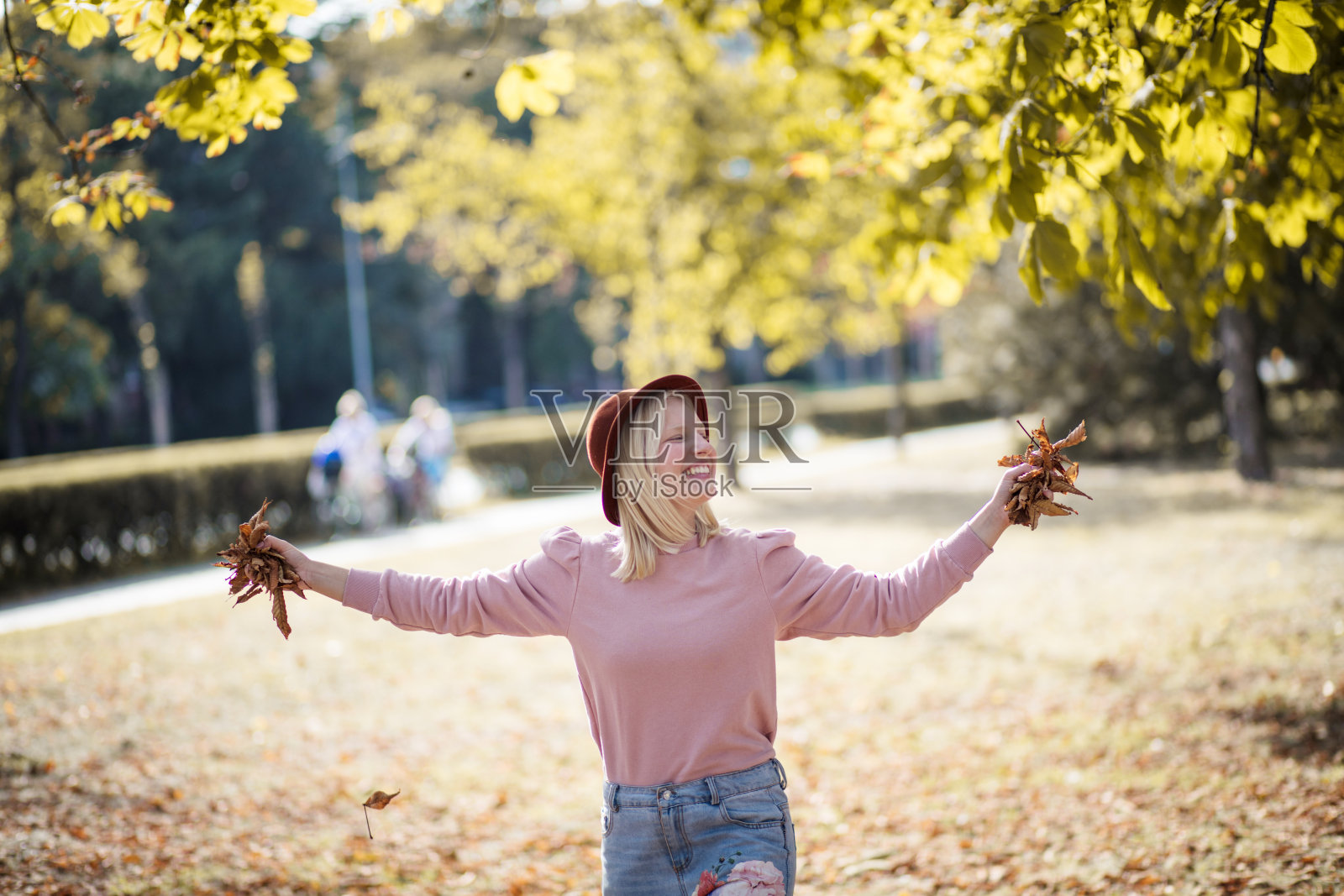 年轻微笑的金发女人在公园里享受着，手里拿着树叶。照片摄影图片