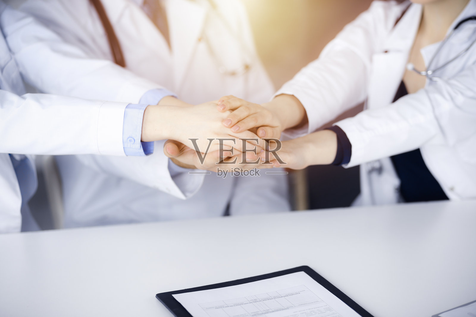 在现代医院的办公室里，一群医生坐在桌子前，手拉手围成一个圈，准备帮助病人。成功的医疗团队，冠状病毒对抗概念照片摄影图片