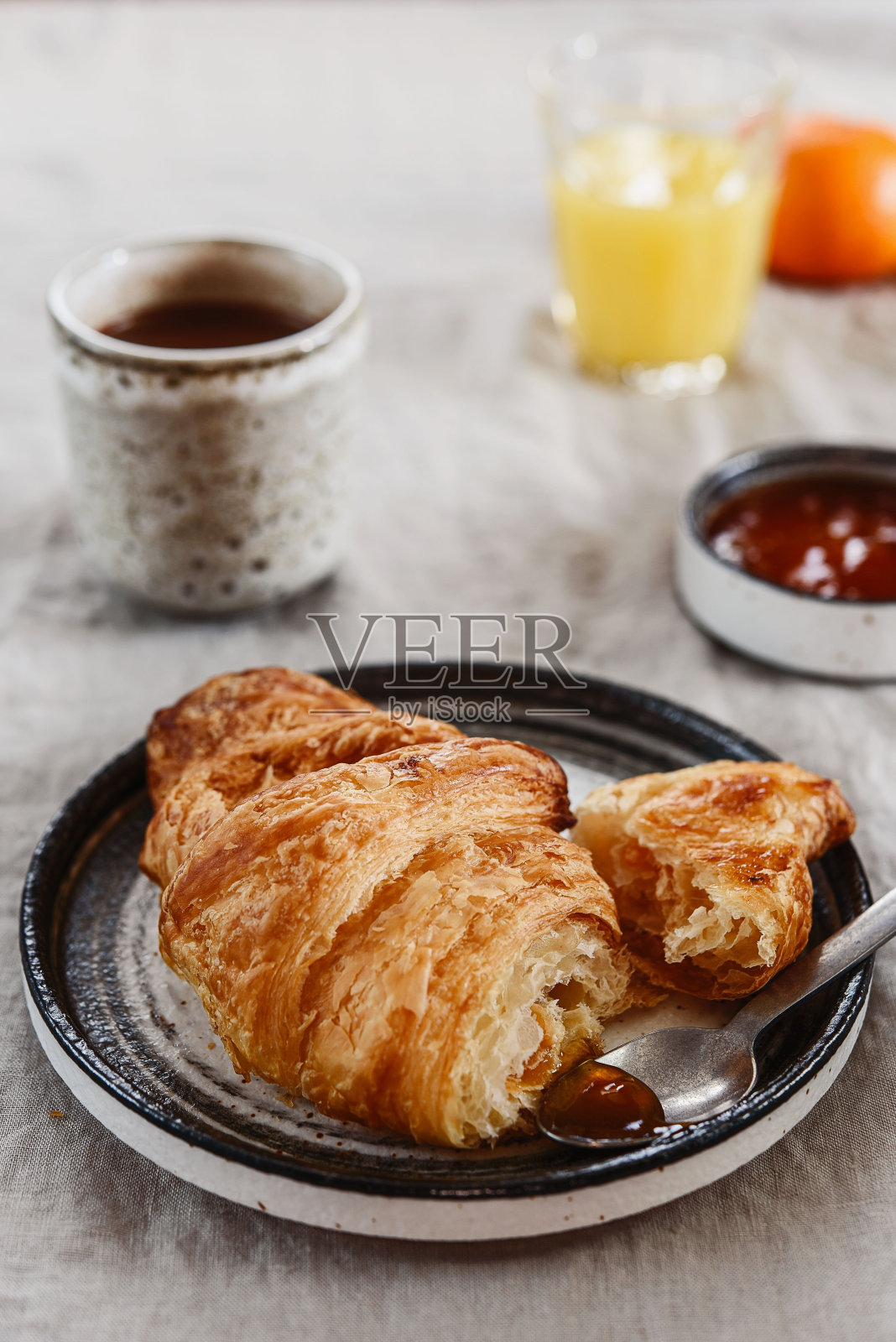 早餐有羊角面包、果酱、热巧克力、果汁和橘黄色桌布照片摄影图片