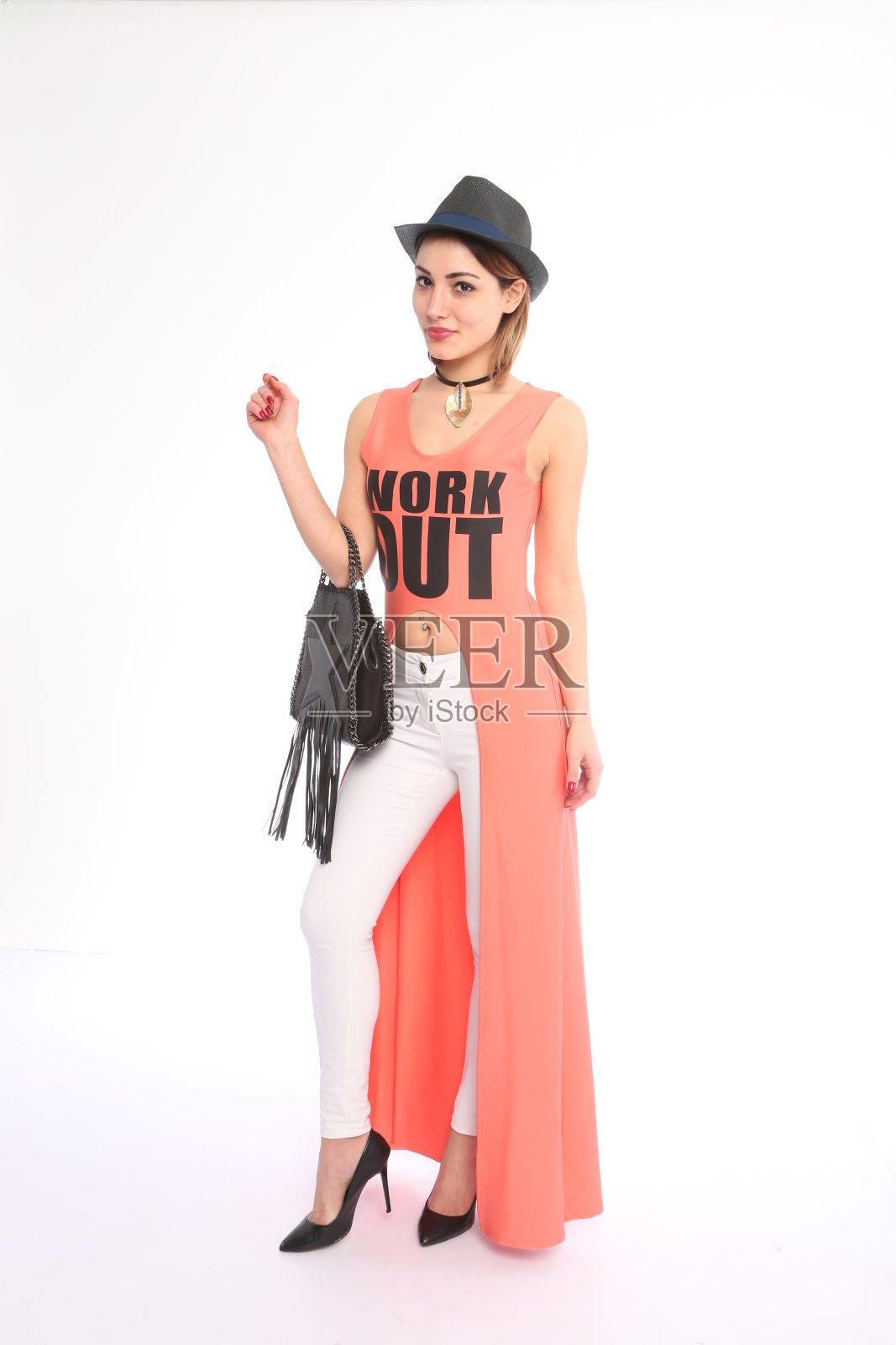 年轻女子戴着帽子，穿着粉色束腰外衣和白色牛仔裤照片摄影图片