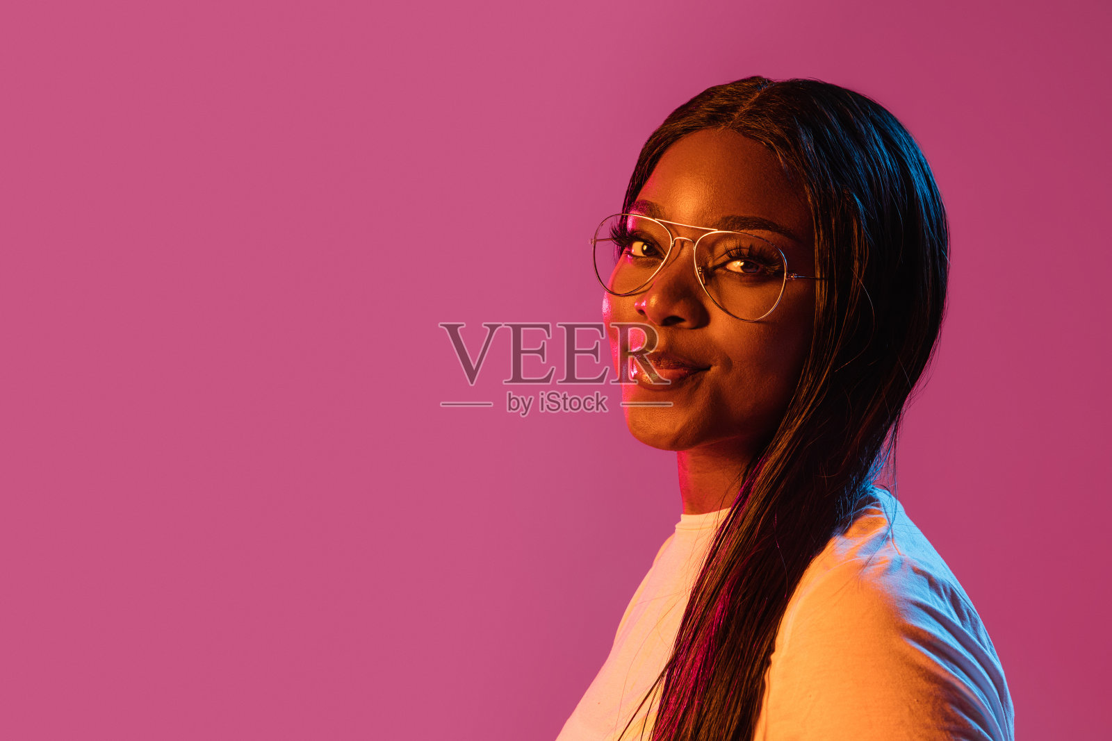 一个非洲年轻女子的肖像，背景是粉红色的霓虹灯。人的情感、面部表情、青春、销售、广告的概念。照片摄影图片