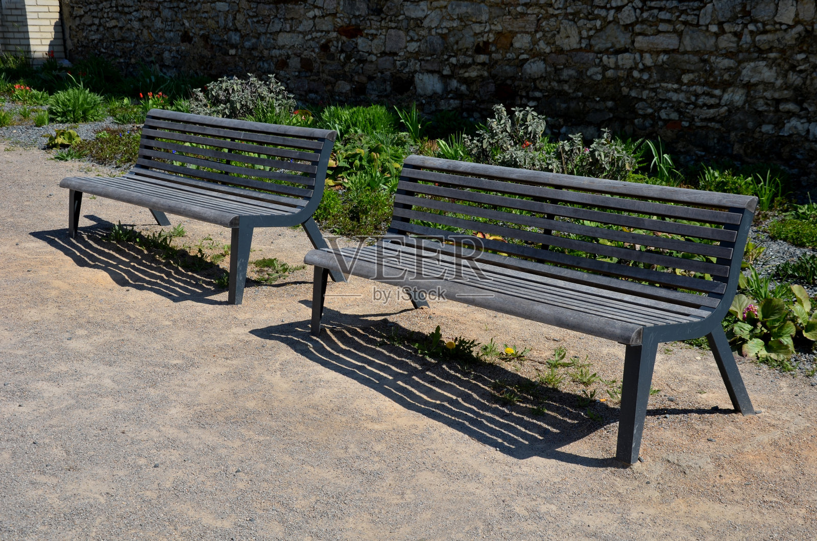 多年生的铺着灰色碎石的床，在石灰石石墙前的广场上，长凳上有木镶板，米色小径由天然米色压实的碎石制成，在春天，照片摄影图片