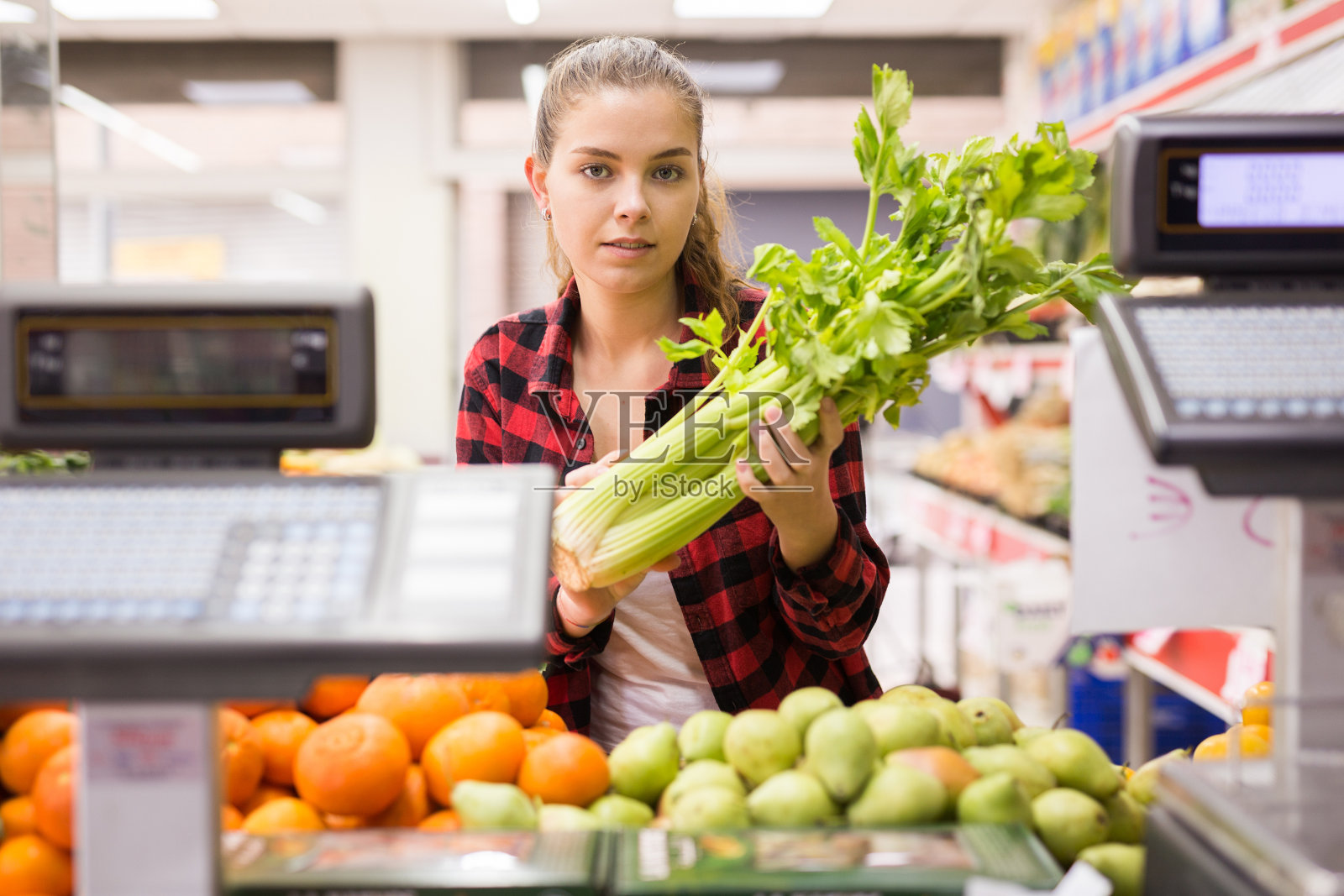 年轻的女顾客站在柜台旁边，手里拿着芹菜照片摄影图片
