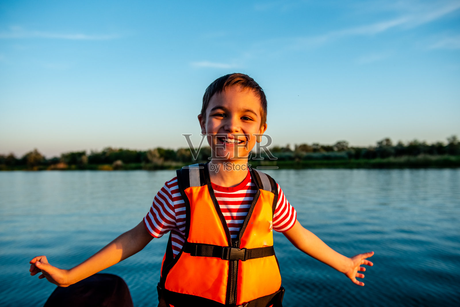 快乐的8岁男孩穿着救生衣在船上走。在湖上度过有趣的假期照片摄影图片