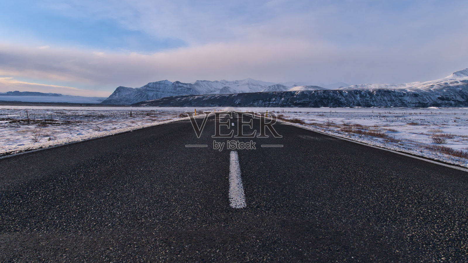 在冬季，冰岛南部Skaftafell附近的空旷的铺砌环线(1号线)和Öræfajökull被雪覆盖的山麓景色逐渐减弱。照片摄影图片
