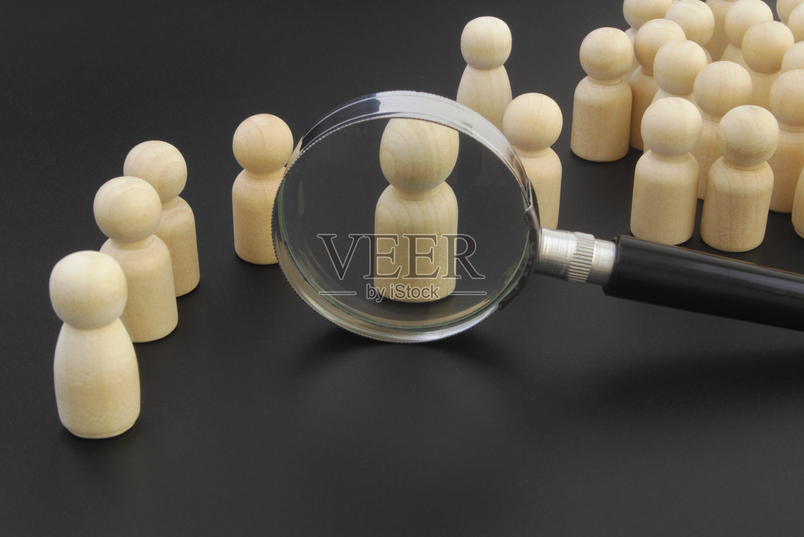 在放大镜下黑色背景上的木制人物。照片摄影图片