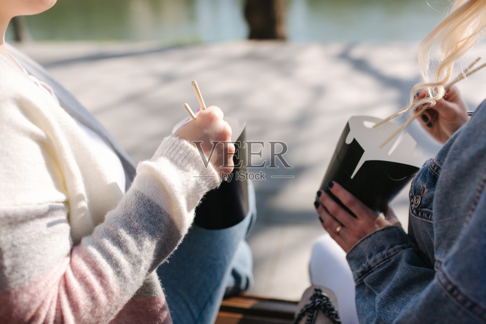 两个吃快餐的漂亮女人。坐在公园长椅上吃亚洲菜的漂亮女孩。外卖食品的概念。手的特写镜头照片摄影图片