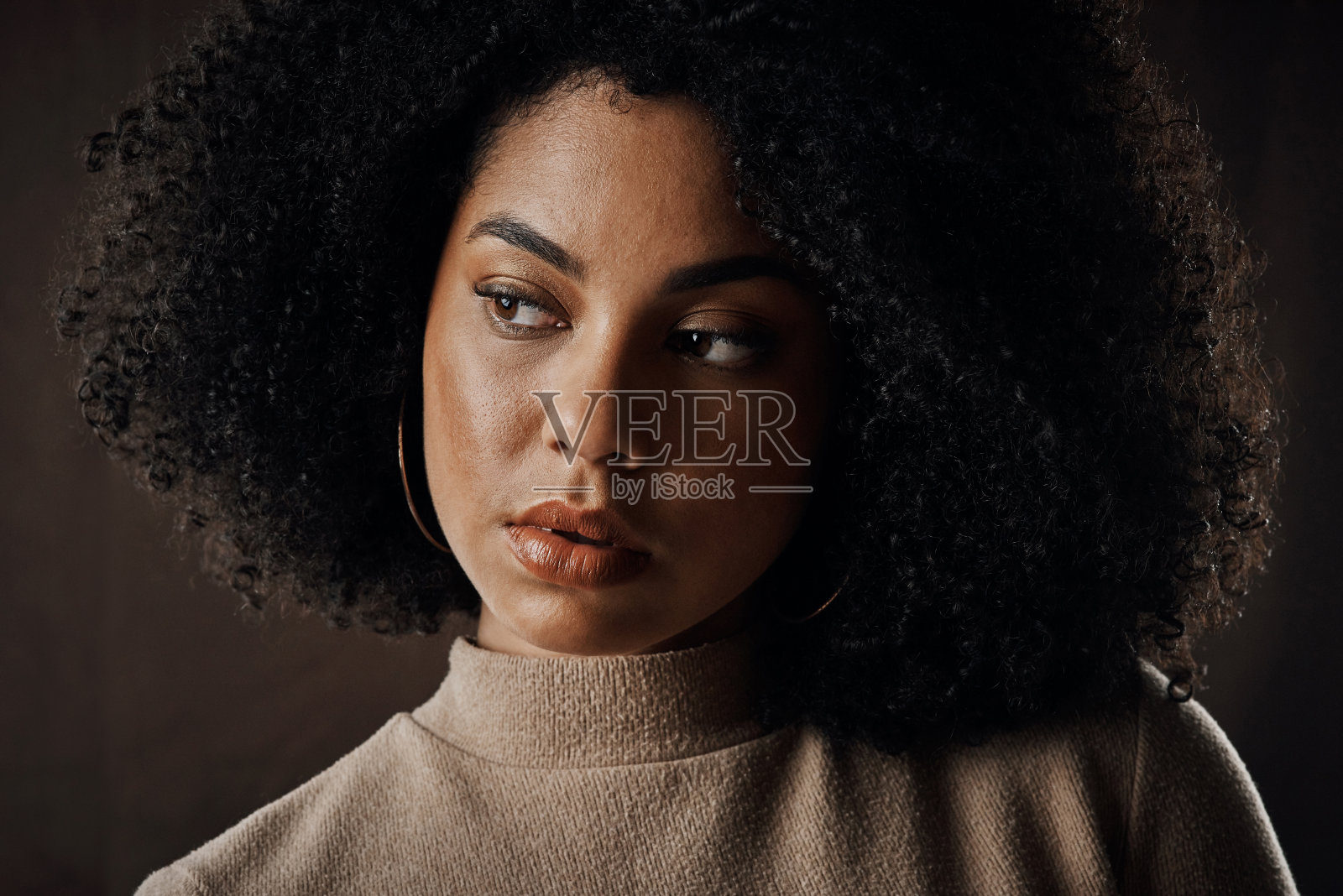 一个漂亮的年轻女子在工作室里以黑暗的背景摆姿势，看起来很有思想照片摄影图片