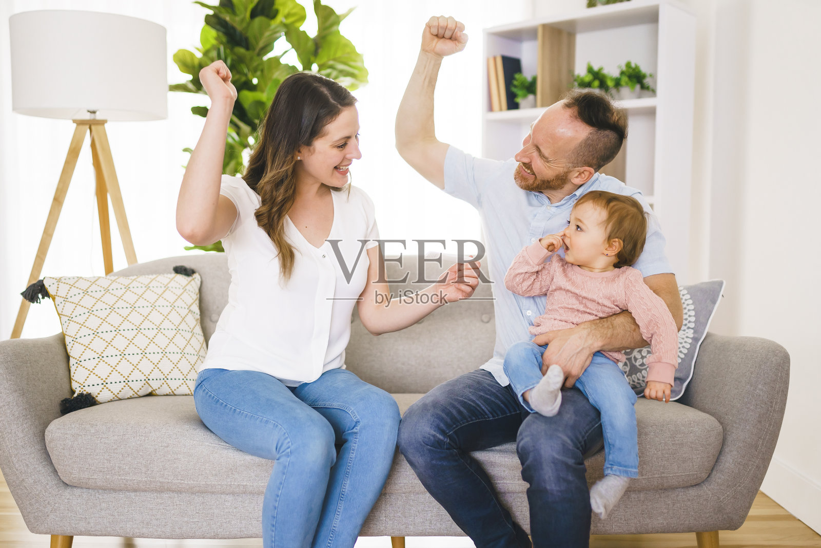 家人开心地拿着验孕棒，兴奋的妻子坐在家里的沙发上。照片摄影图片