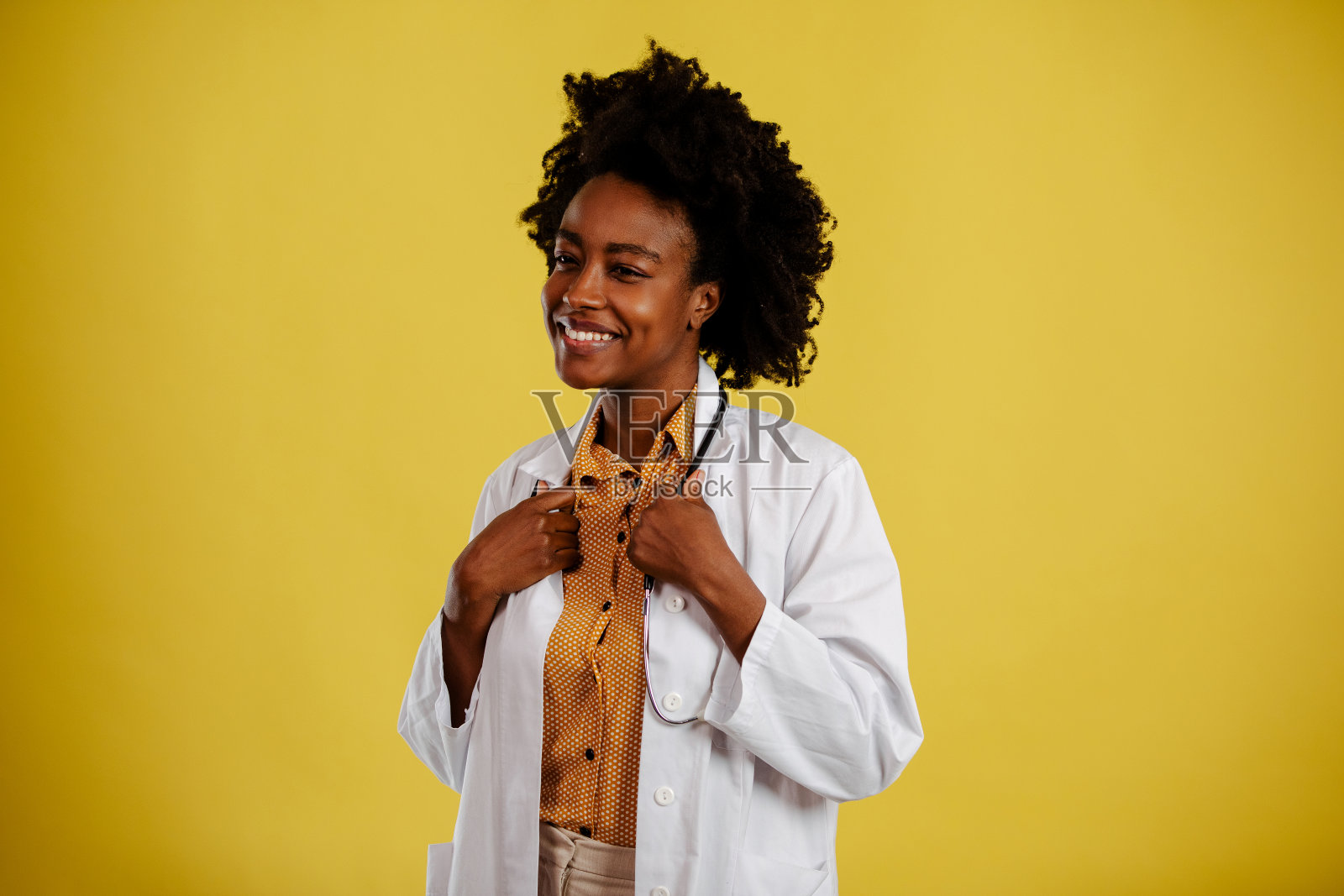 黄色背景上的年轻美国黑人医生的肖像。医生拿着听诊器。照片摄影图片