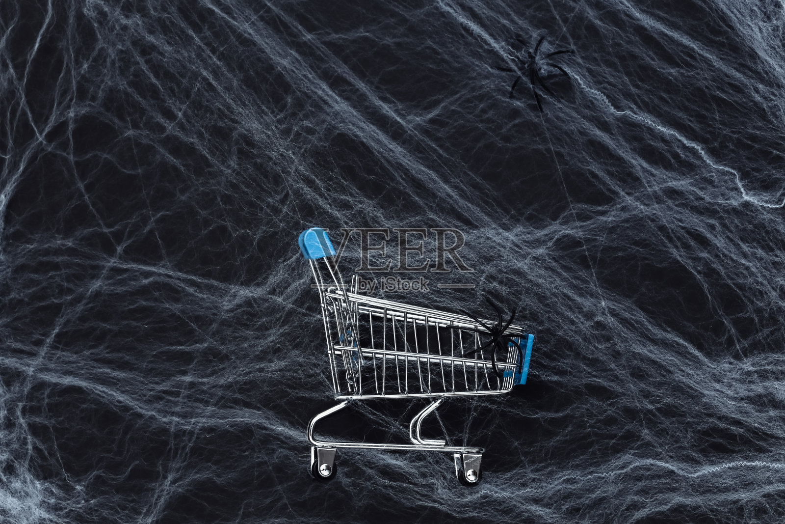 万圣节销售、购物。黑色背景的超市手推车上有蜘蛛网和蜘蛛。万圣节装饰。俯视图照片摄影图片