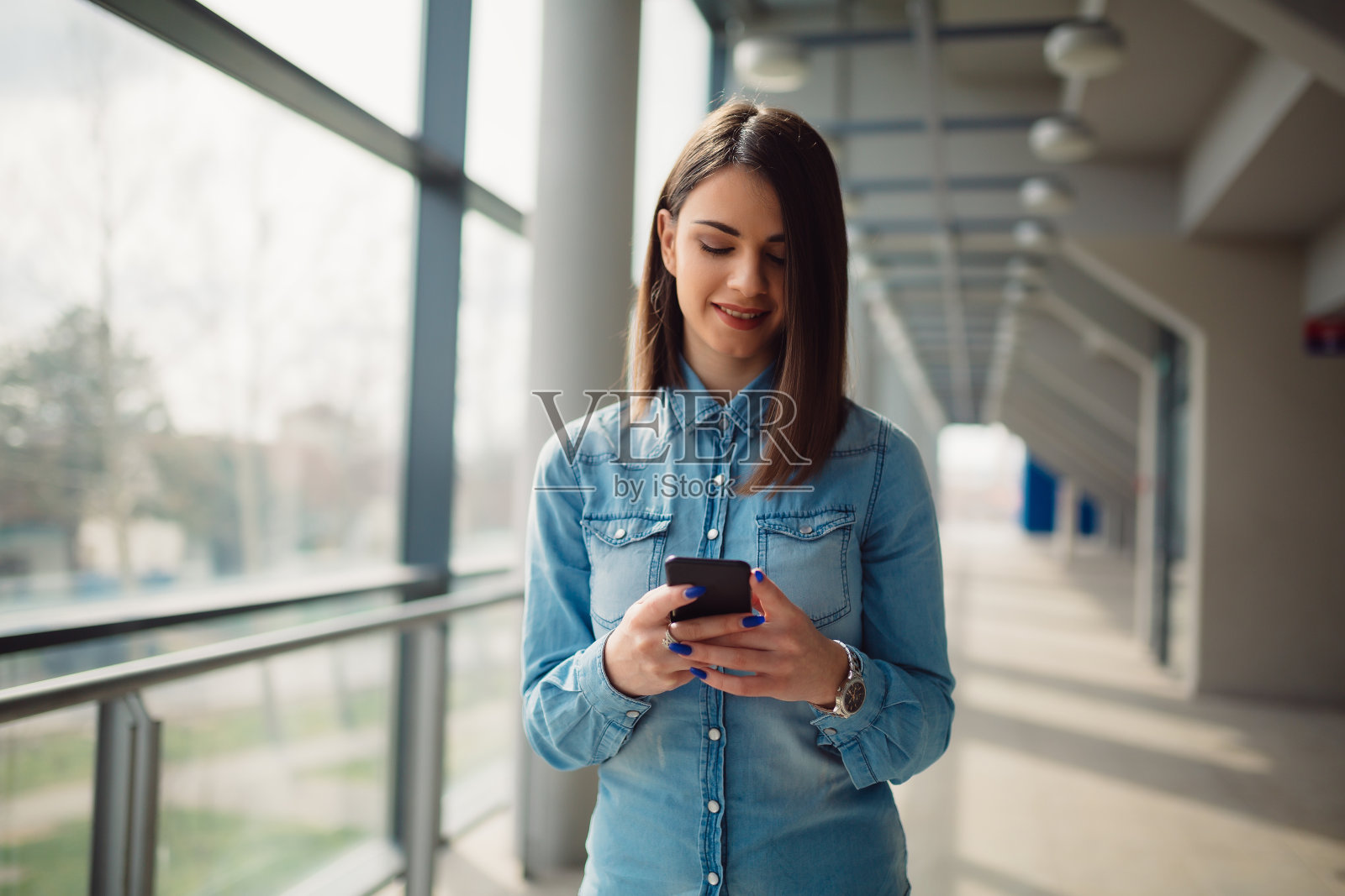 穿着德州衬衫的黑发美女正在用她的智能手机发送信息照片摄影图片