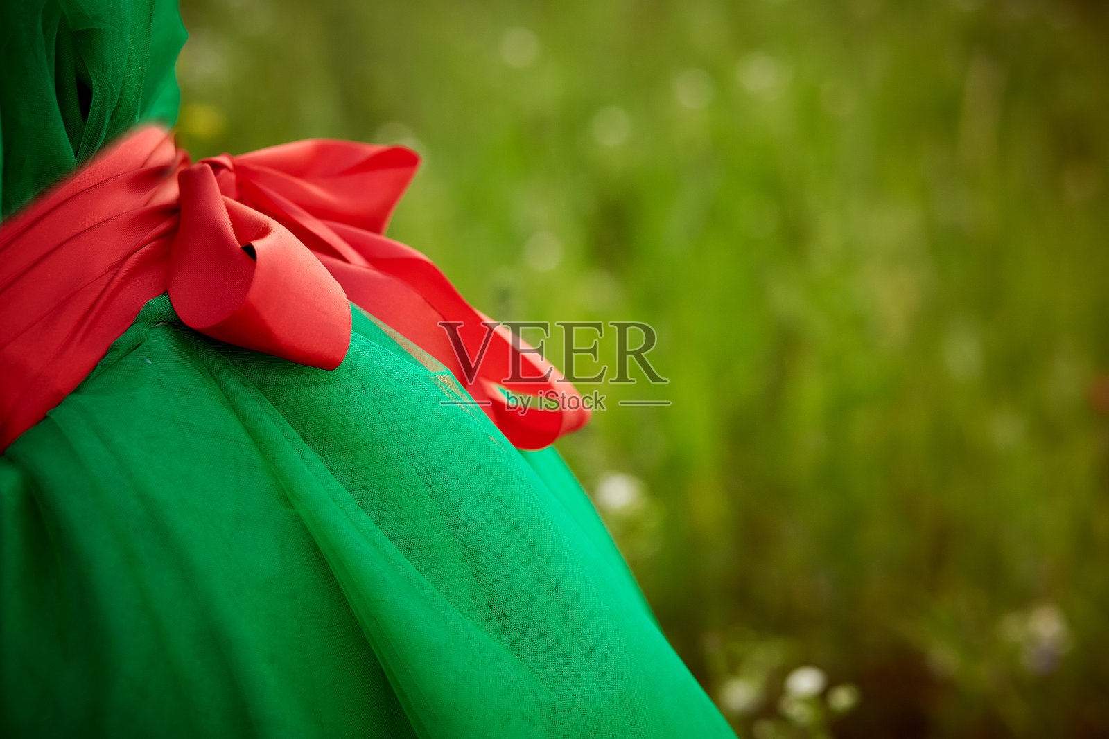 在绿色田野的背景上，穿着绿色裙子带着红色蝴蝶结的女孩。夏天背景的概念。本空间照片摄影图片