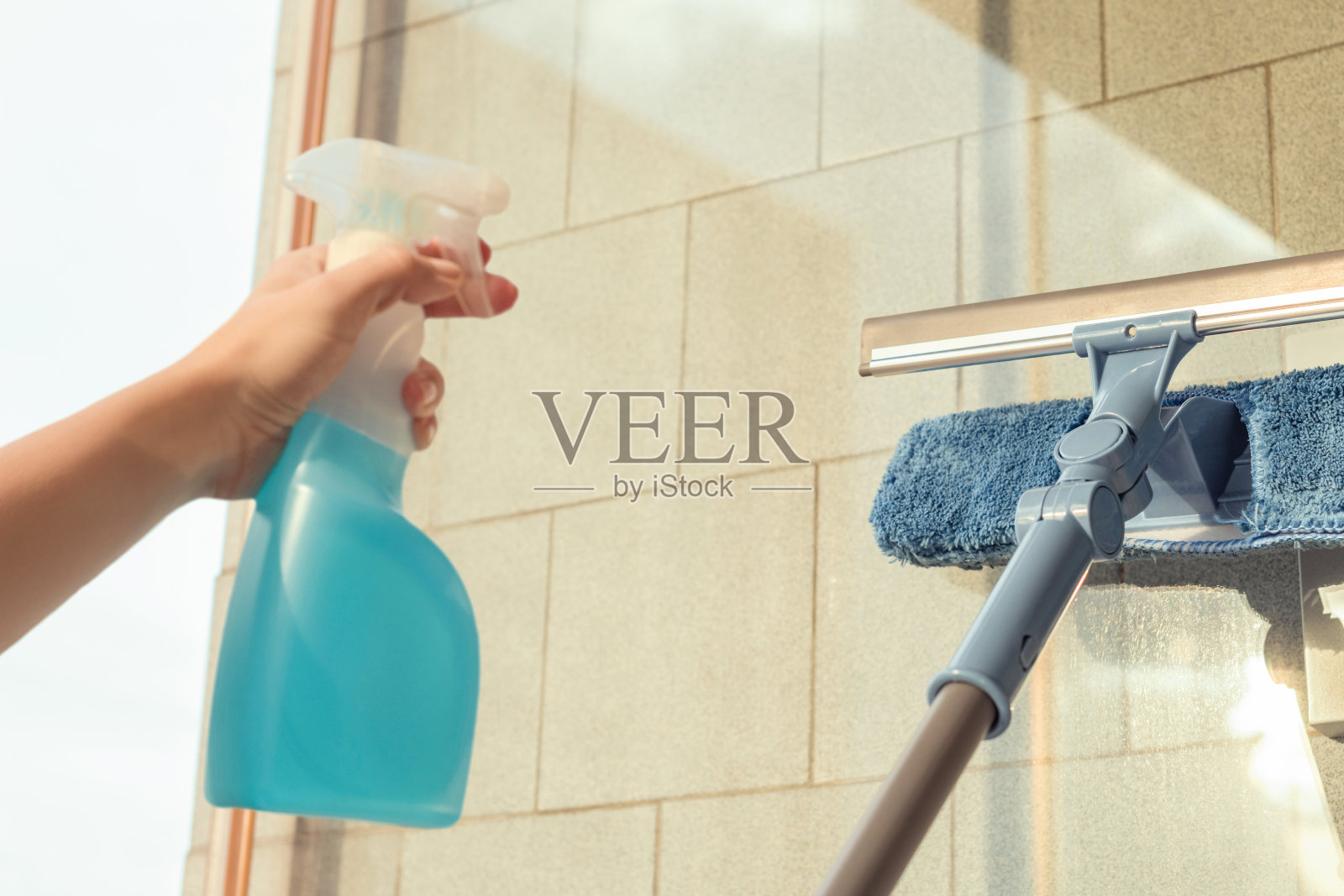 妇女在夏日黄昏，喷洒清洁用品，用拖把海绵擦拭阳台窗户。照片摄影图片