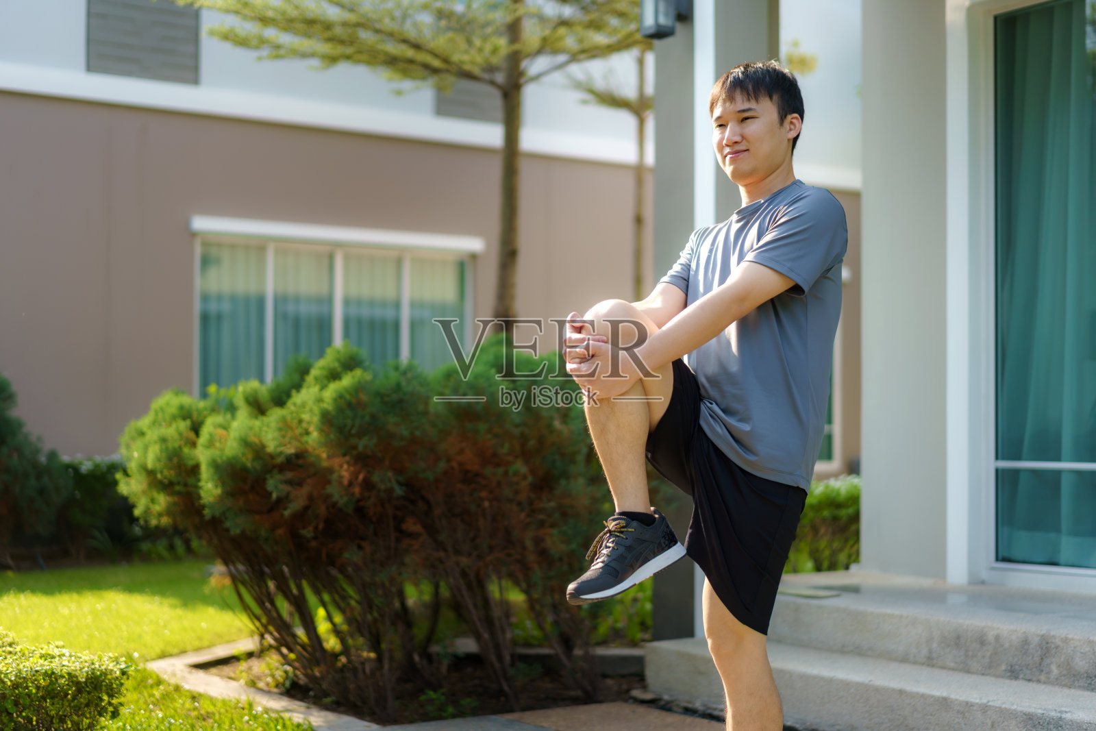 亚洲男人伸展运动前或运动后，在邻居家的前门附近，为身体和精神上的健康和幸福做热身或降温运动。照片摄影图片