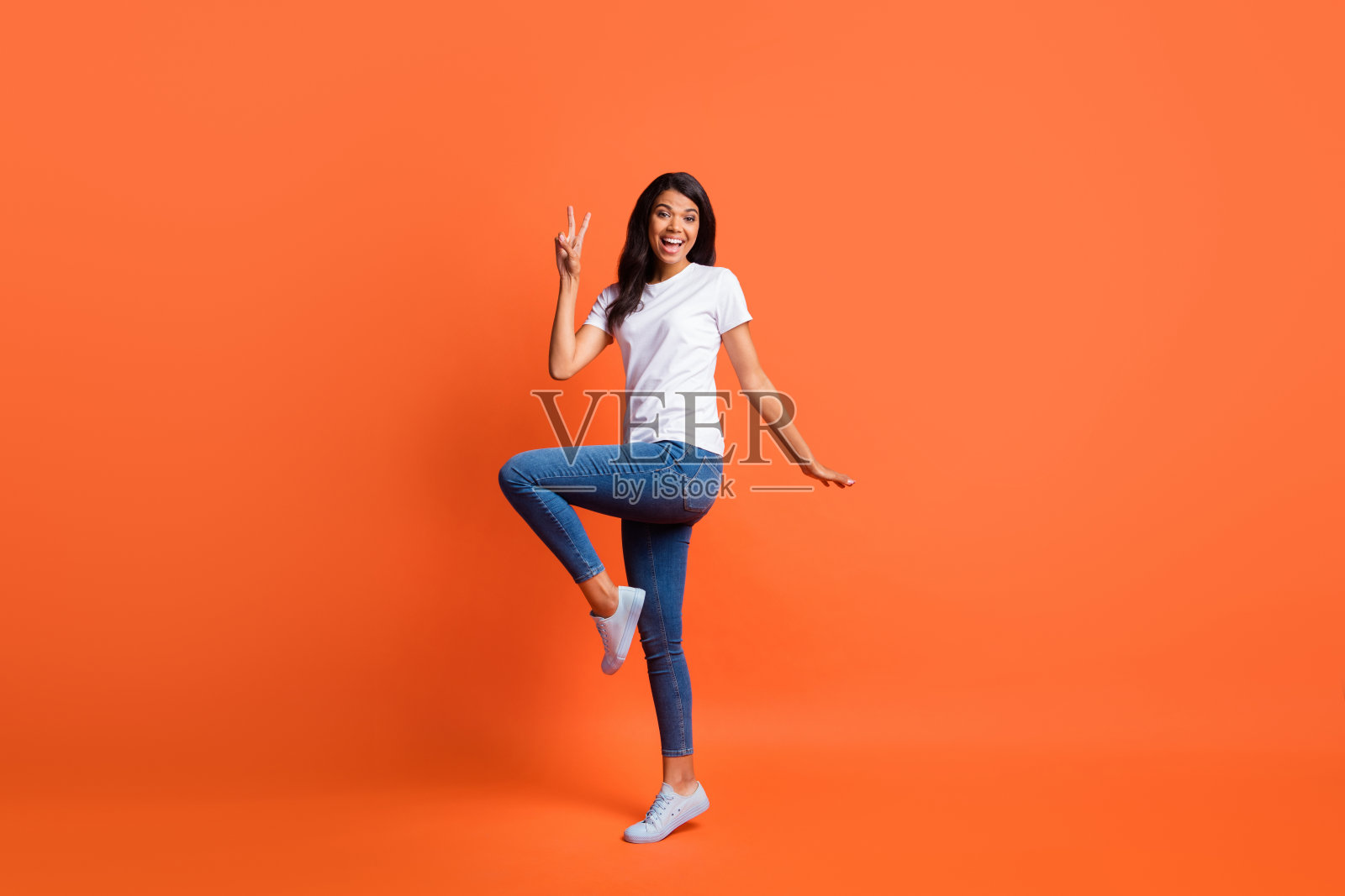 全长照片的女士显示v字张嘴穿白色t恤牛仔裤鞋孤立的橙色背景照片摄影图片