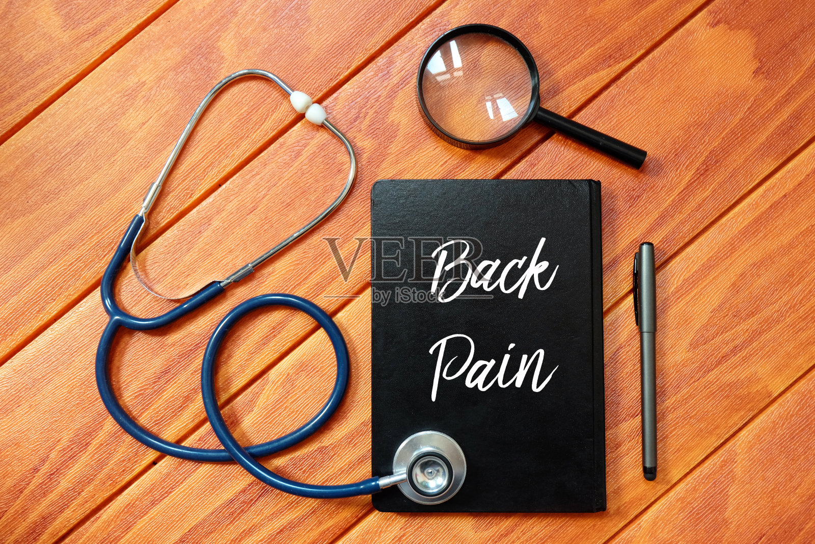 听诊器俯视图，放大镜，笔和笔记本上写的背痛在木制背景。健康的概念。照片摄影图片