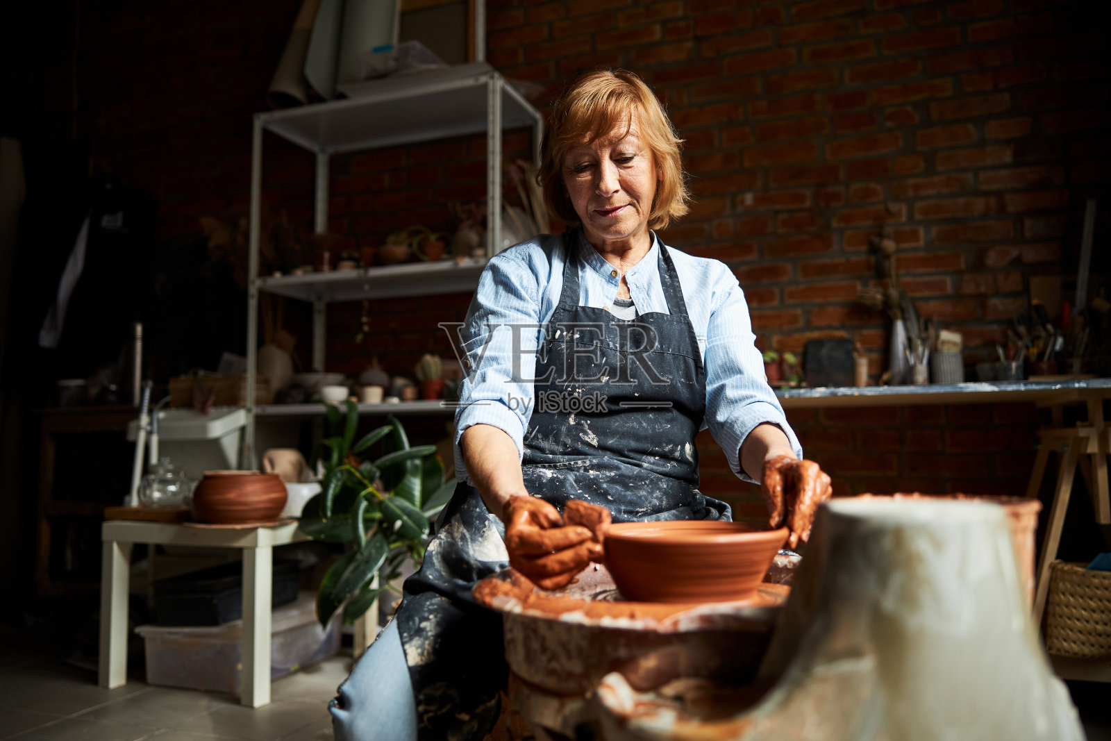 在陶艺工坊里做陶罐的漂亮老妇人照片摄影图片