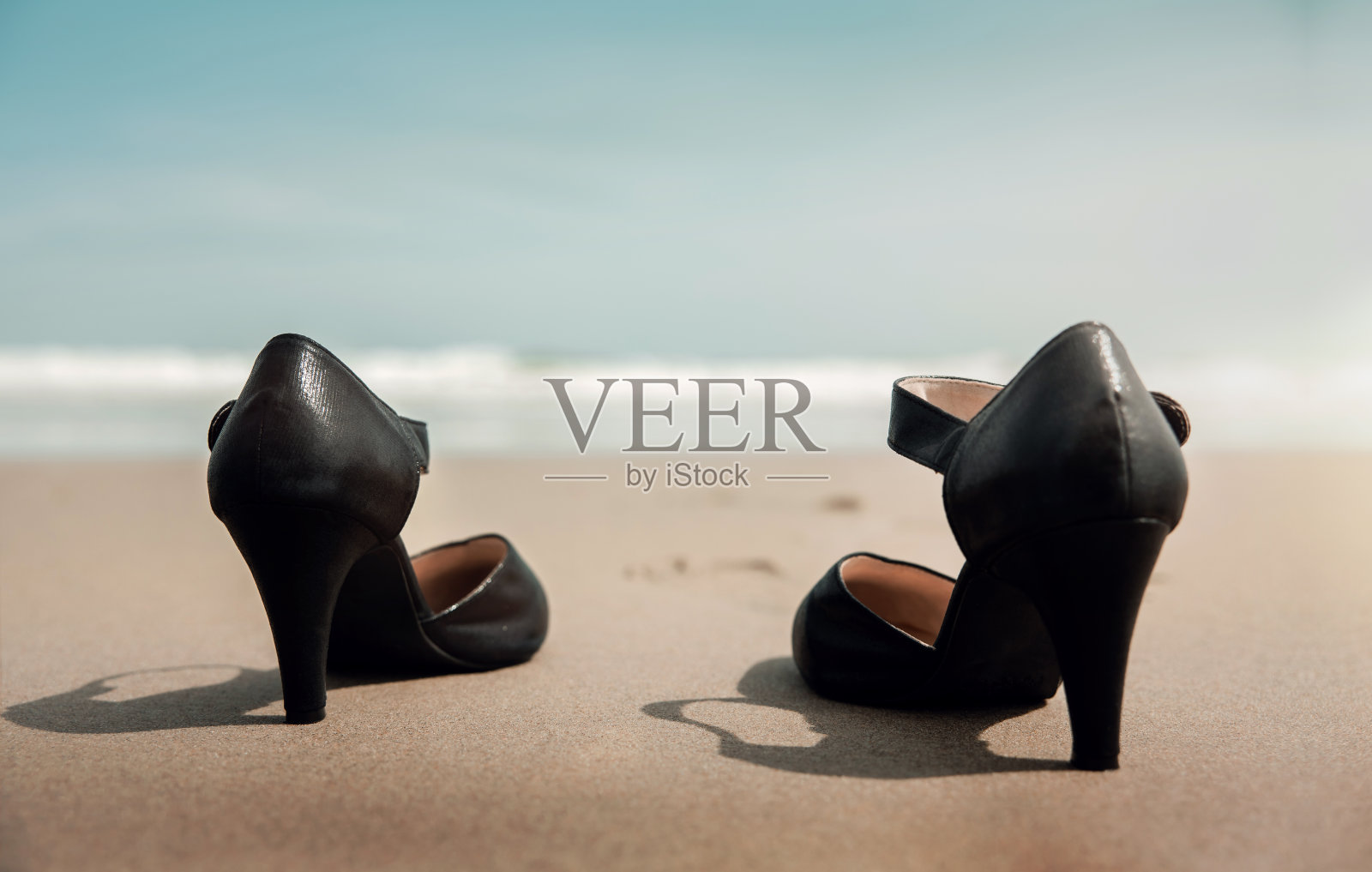 平衡工作与生活的理念。在阳光明媚的日子里，女商人把她的工作鞋脱下放在沙滩上，走进大海。辞掉工作、去办公室郊游或暑假。低角度的观点照片摄影图片