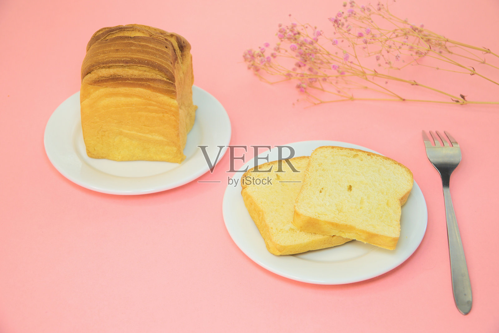 粉色背景上放着两盘面包片和一把勺子照片摄影图片